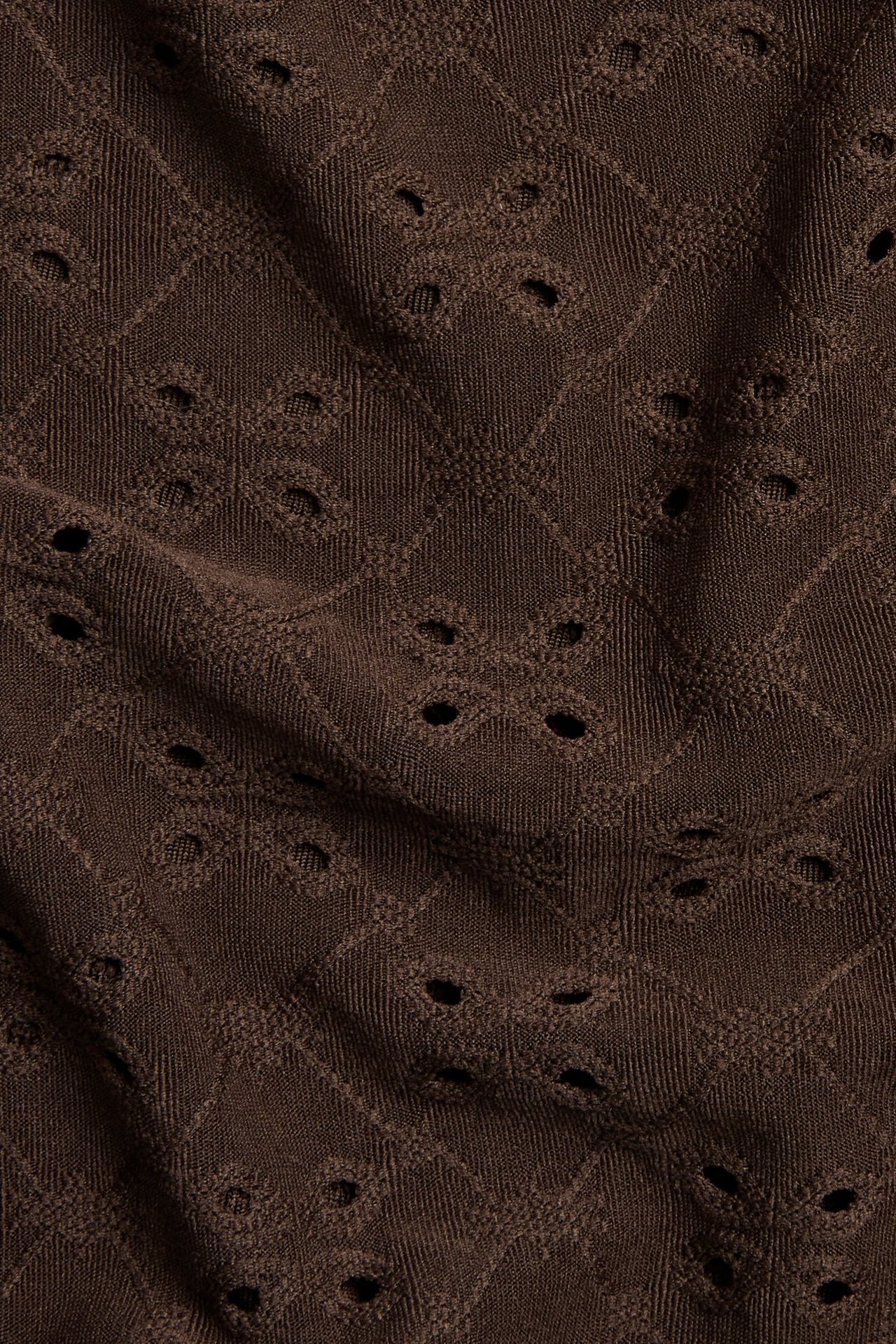 Lähikuva tummanruskeasta jacquard-topista, jossa on broderie anglaise -kuvioita.