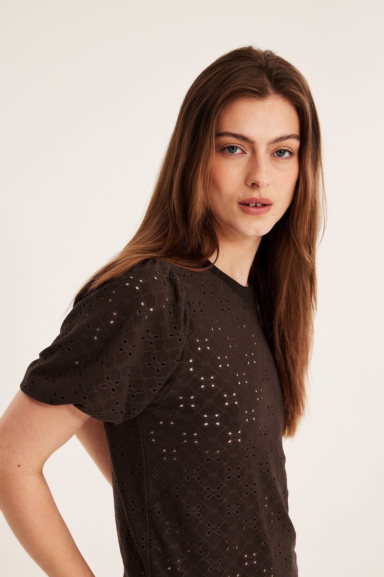 Närbild på kvinna i mörkbrun broderie anglaise topp med puffärm.