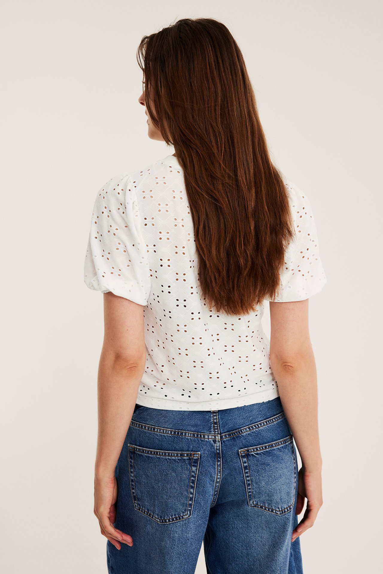 Ryggvy av en kvinna i offwhite broderie anglaise puffärmstopp och blå jeans.