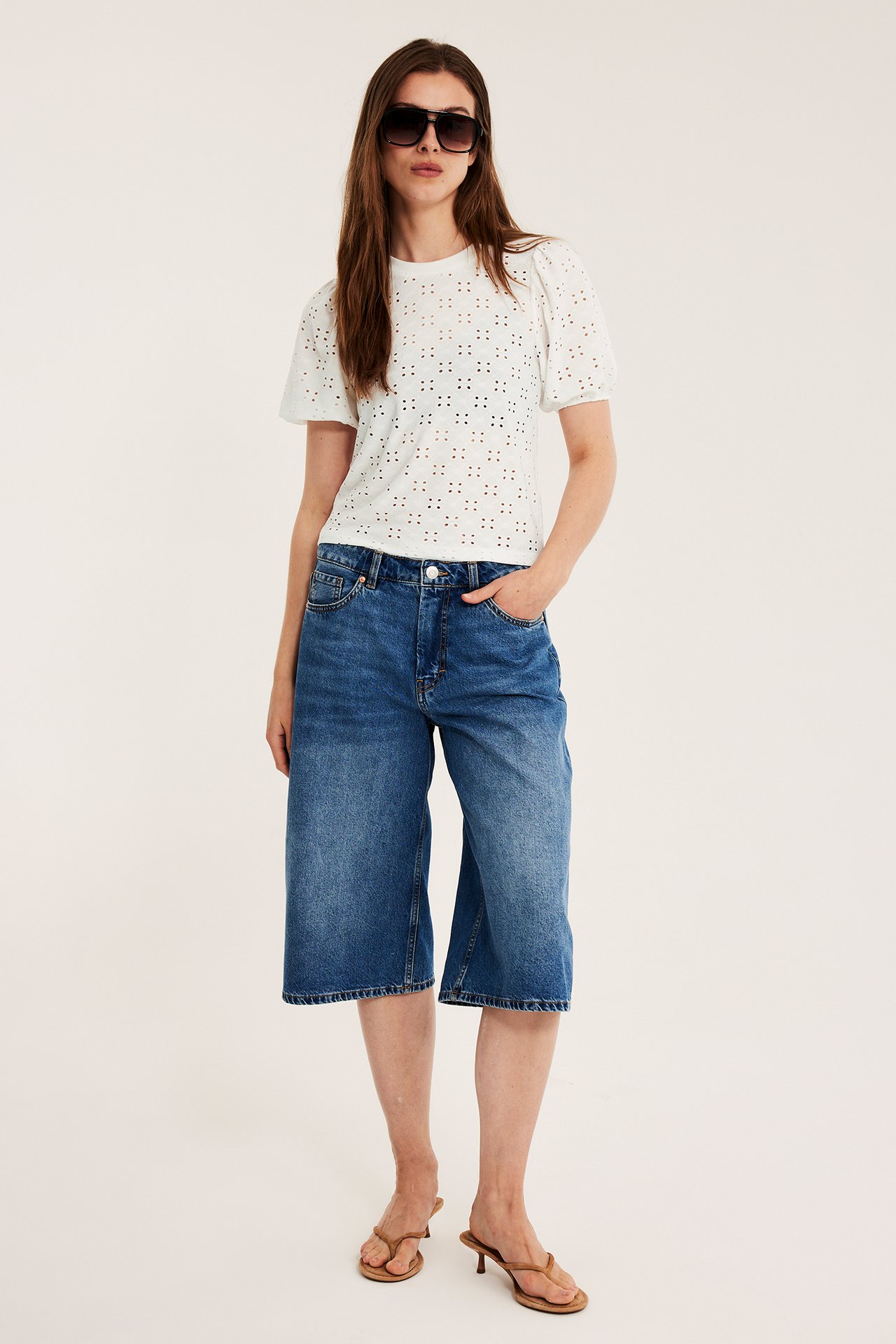 Framifrån: Offwhite broderie anglaise puffärmstopp, blå jeansculottes, bruna sandaler och solglasögon.