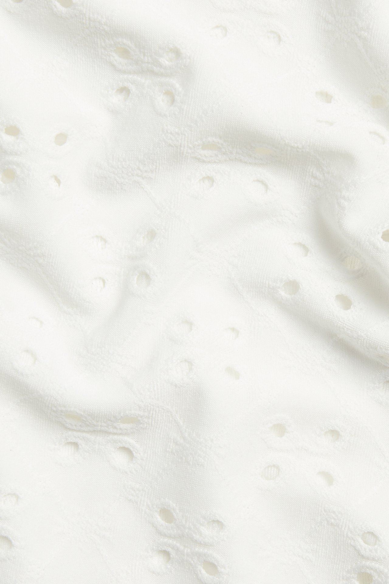Zbliżenie na białawą tkaninę broderie anglaise z żakardowym wzorem na top.