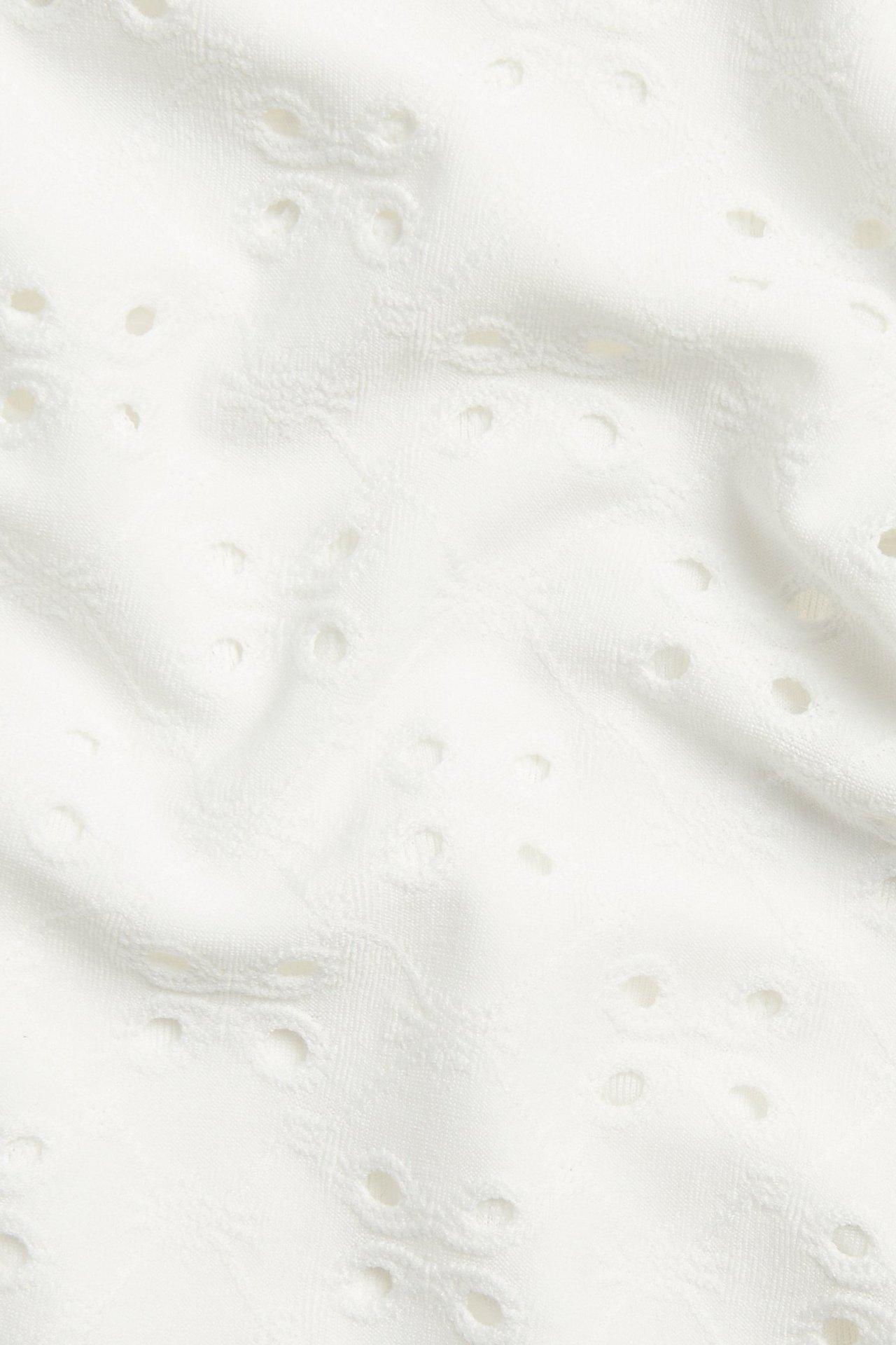 Lähikuva luonnonvalkoisesta brodeeratusta batistista, jossa jacquardkuviointi toppiin.