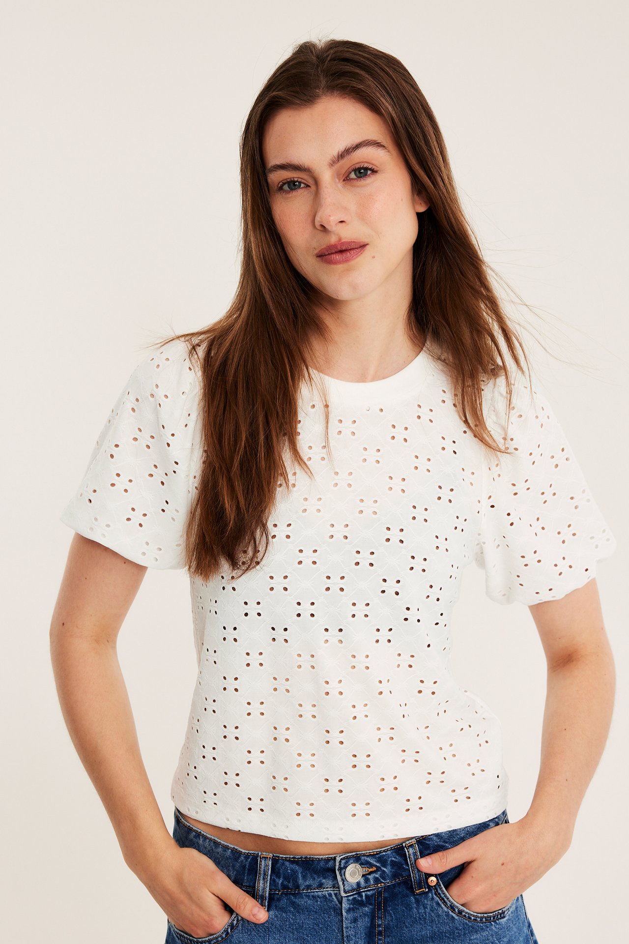 Framifrån: kvinna i offwhite topp med broderie anglaise, puffärmar och blå jeans.