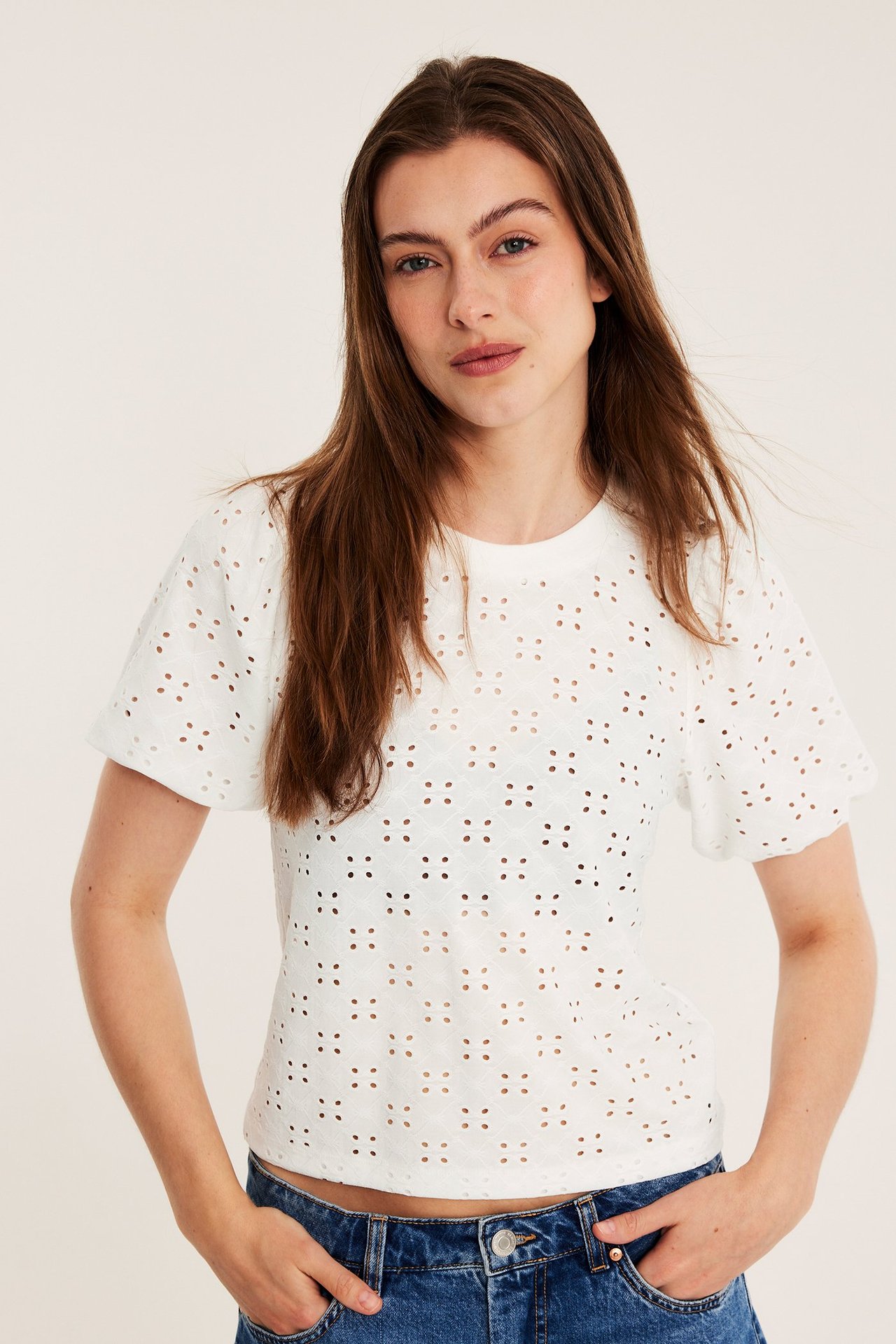 Edestä kuvattuna nainen yllään luonnonvalkoinen brodeerattu pusero pöyhkeillä hihoilla ja siniset farkut.