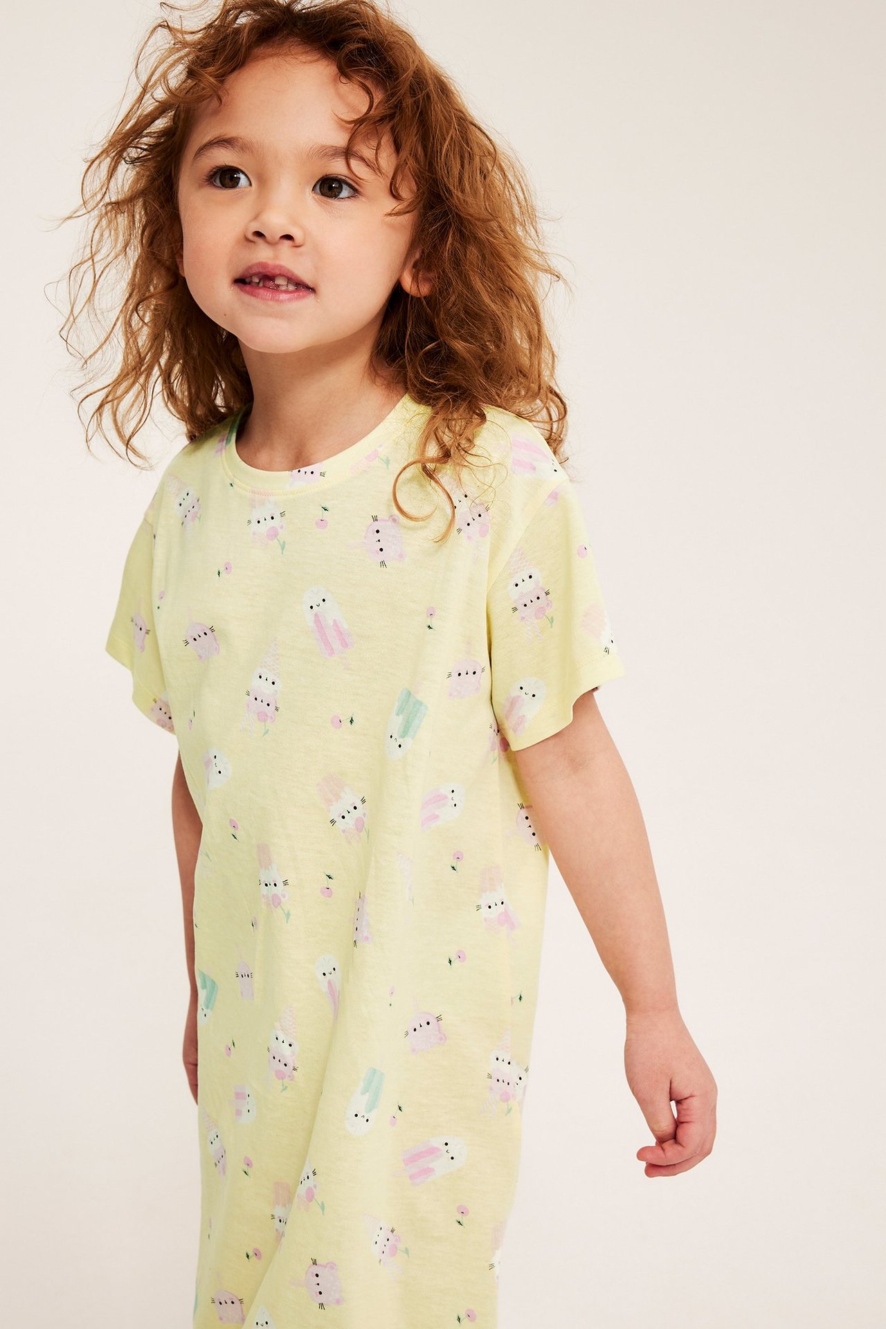 Widok z przodu: dziecko w jasnożółtej, bawełnianej koszuli nocnej z krótkim rękawem i wzorem lodów.