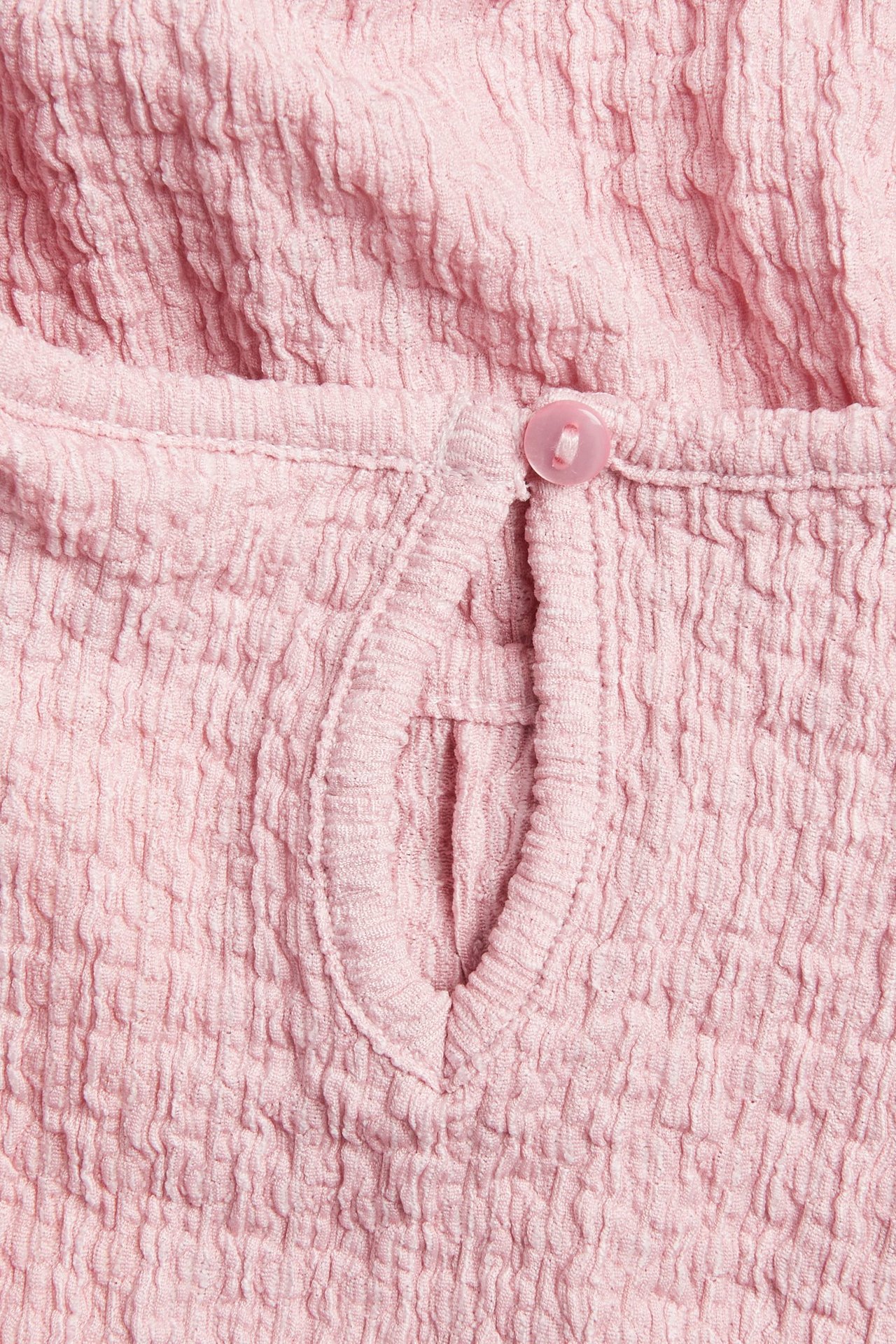Nærbilde av lys rosa krøllet jerseykjole med nøkkelhullsåpning og knappelukking.