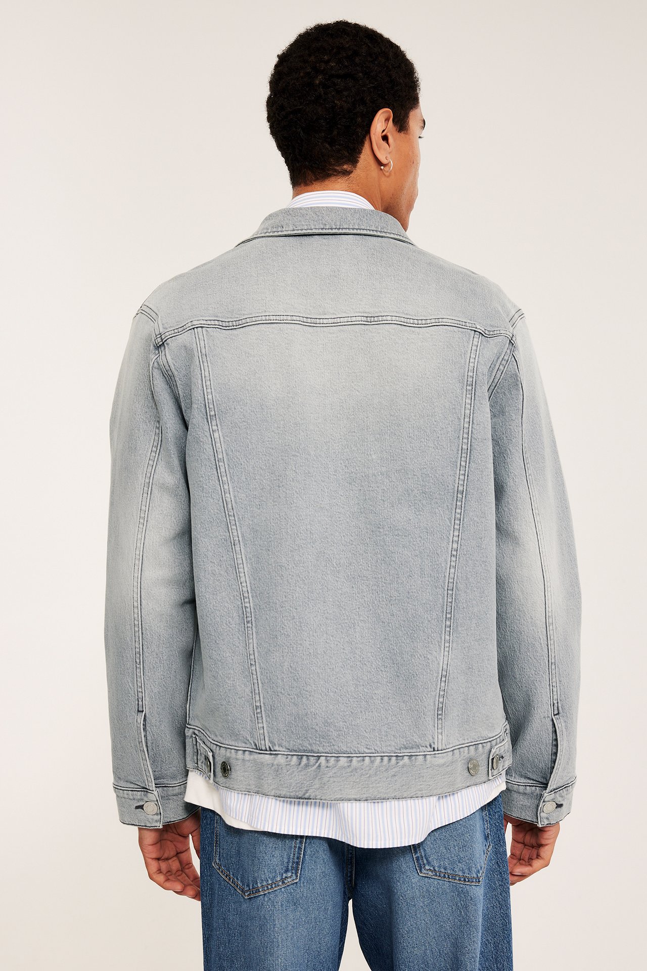 Bakfra: En mann i lys grå dongerijakke over en stripet skjorte og blå jeans.