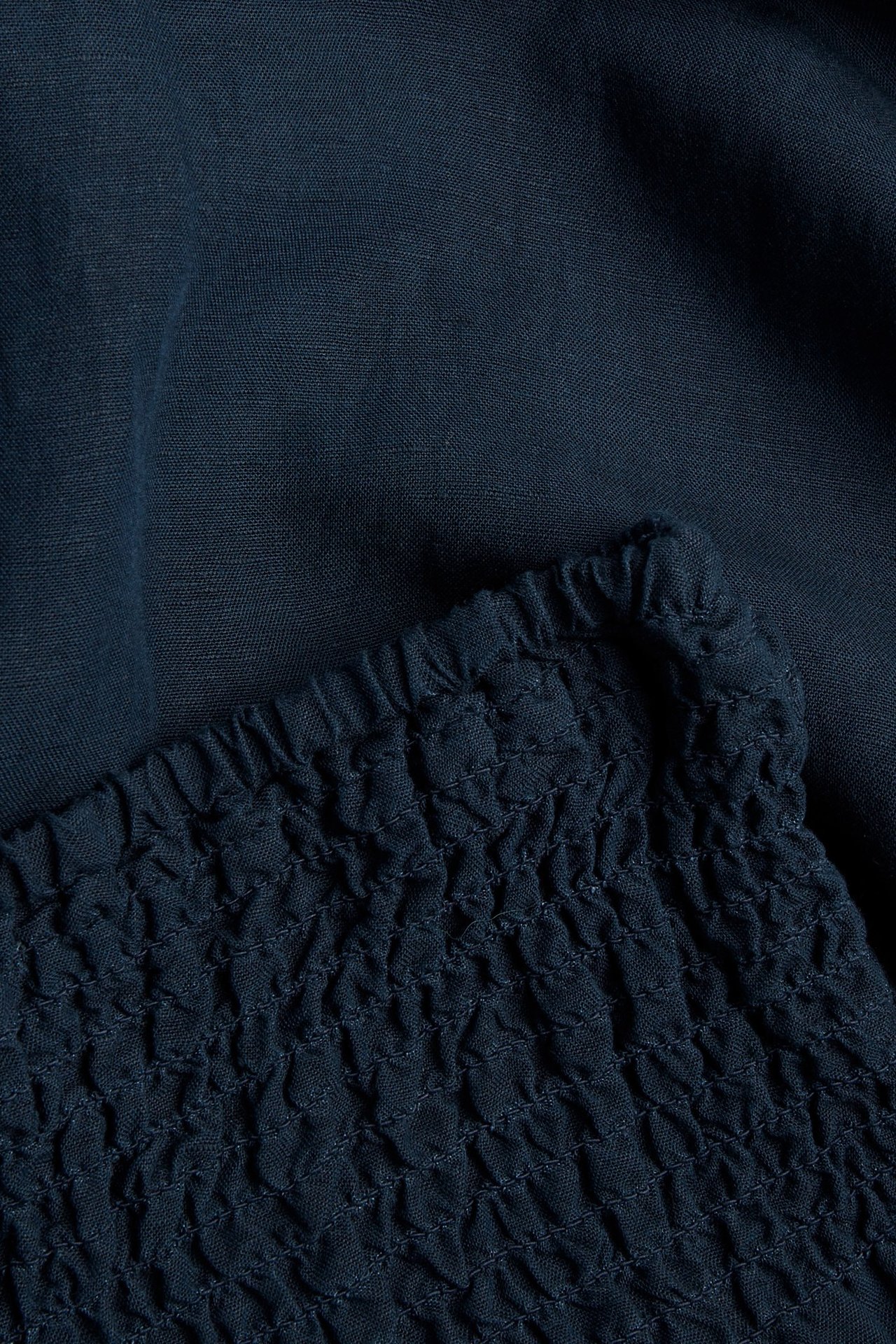 Zbliżenie na ciemnoniebieskie spodnie z mieszanki lnu i wiskozy ze ściągaczem w pasie.