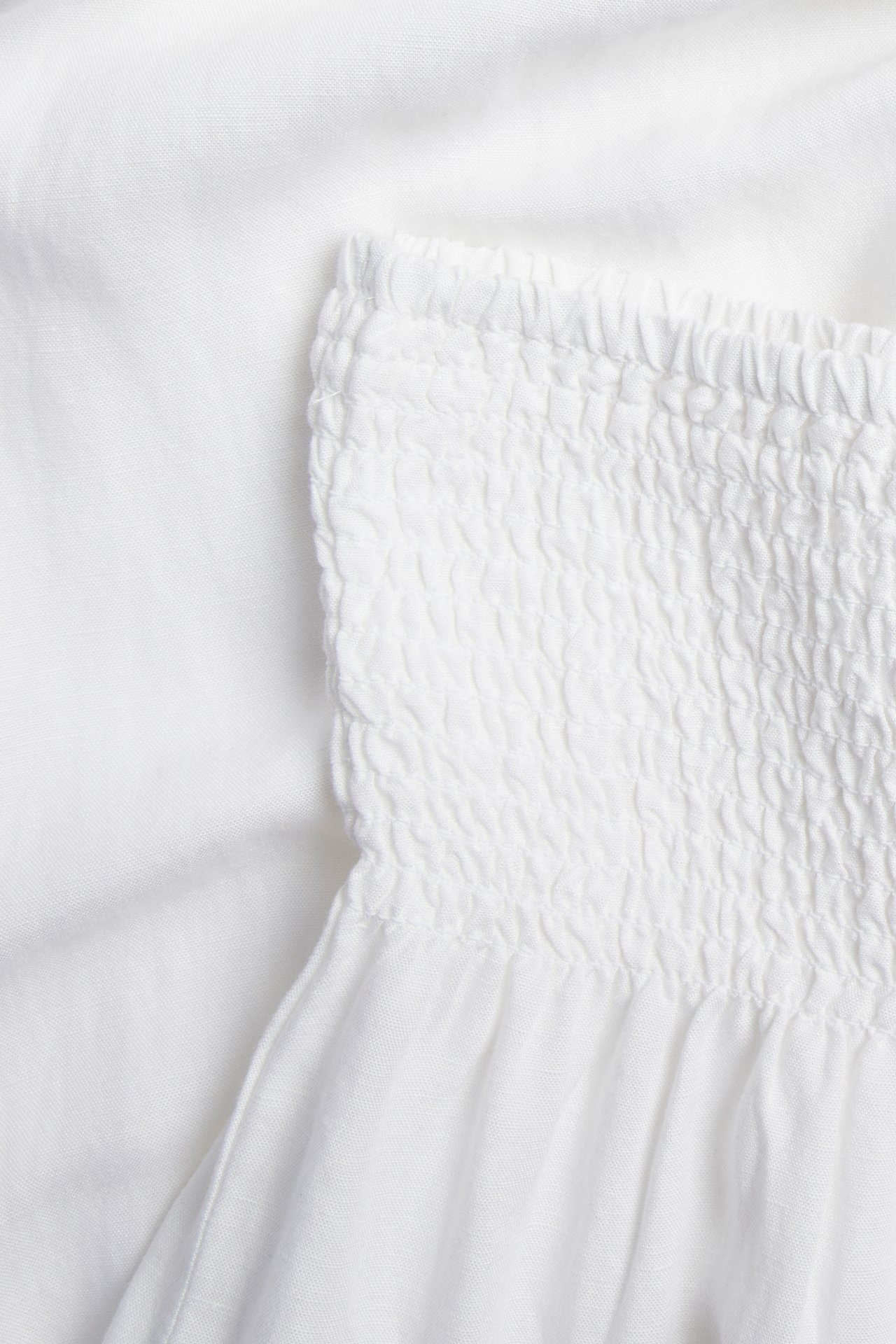 Lähikuva valkoisista pellavasekoitehousuista, joissa on smokkivyötärö.