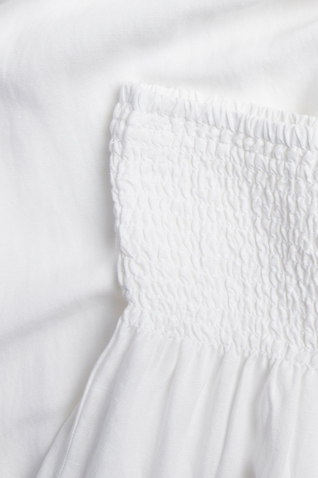 Lähikuva valkoisista pellavasekoitehousuista, joissa on smokkivyötärö.