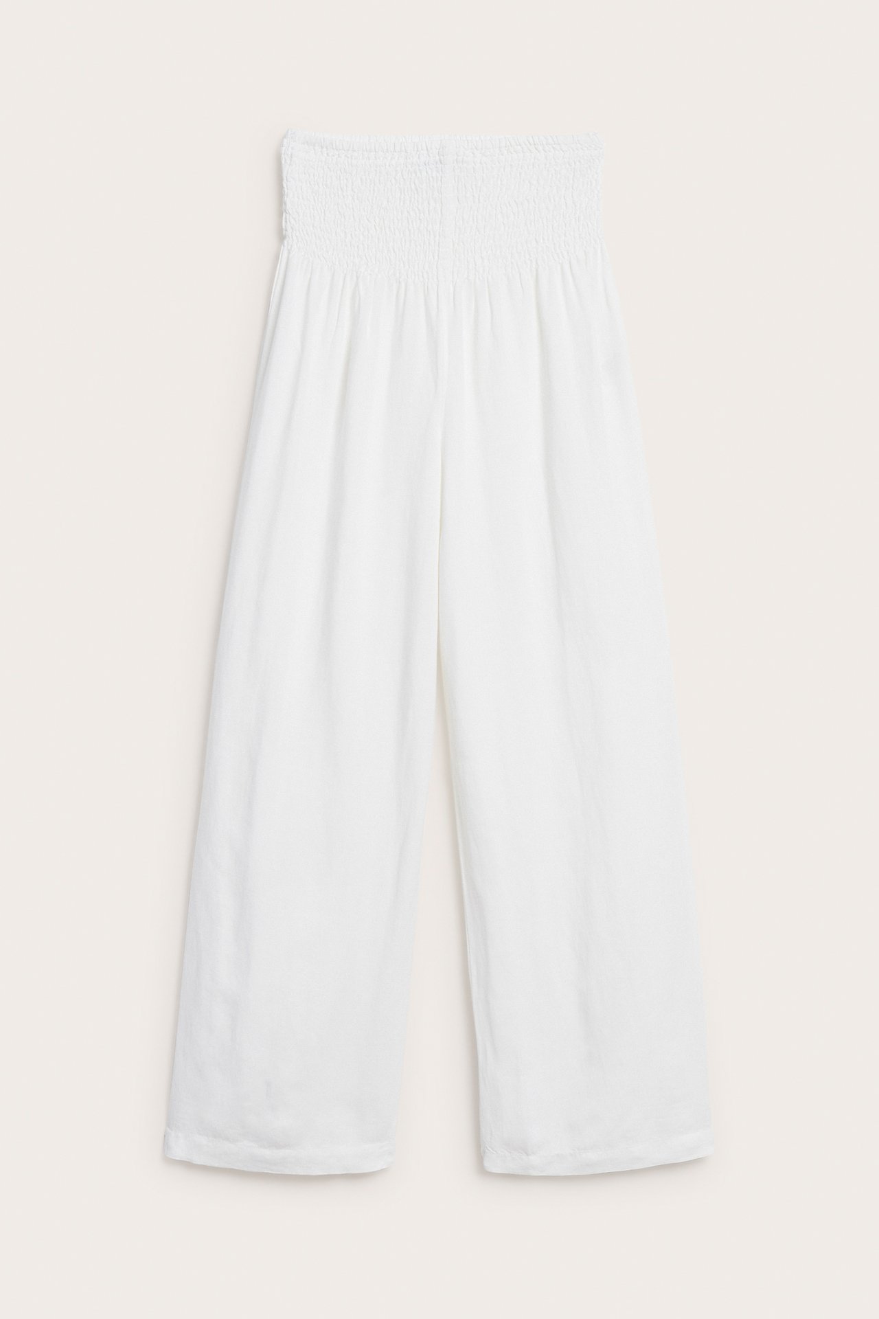 Edestäpäin valkoiset leveälahkeiset pellavasekoitehousut, joissa smokkirypytys vyötäröllä.