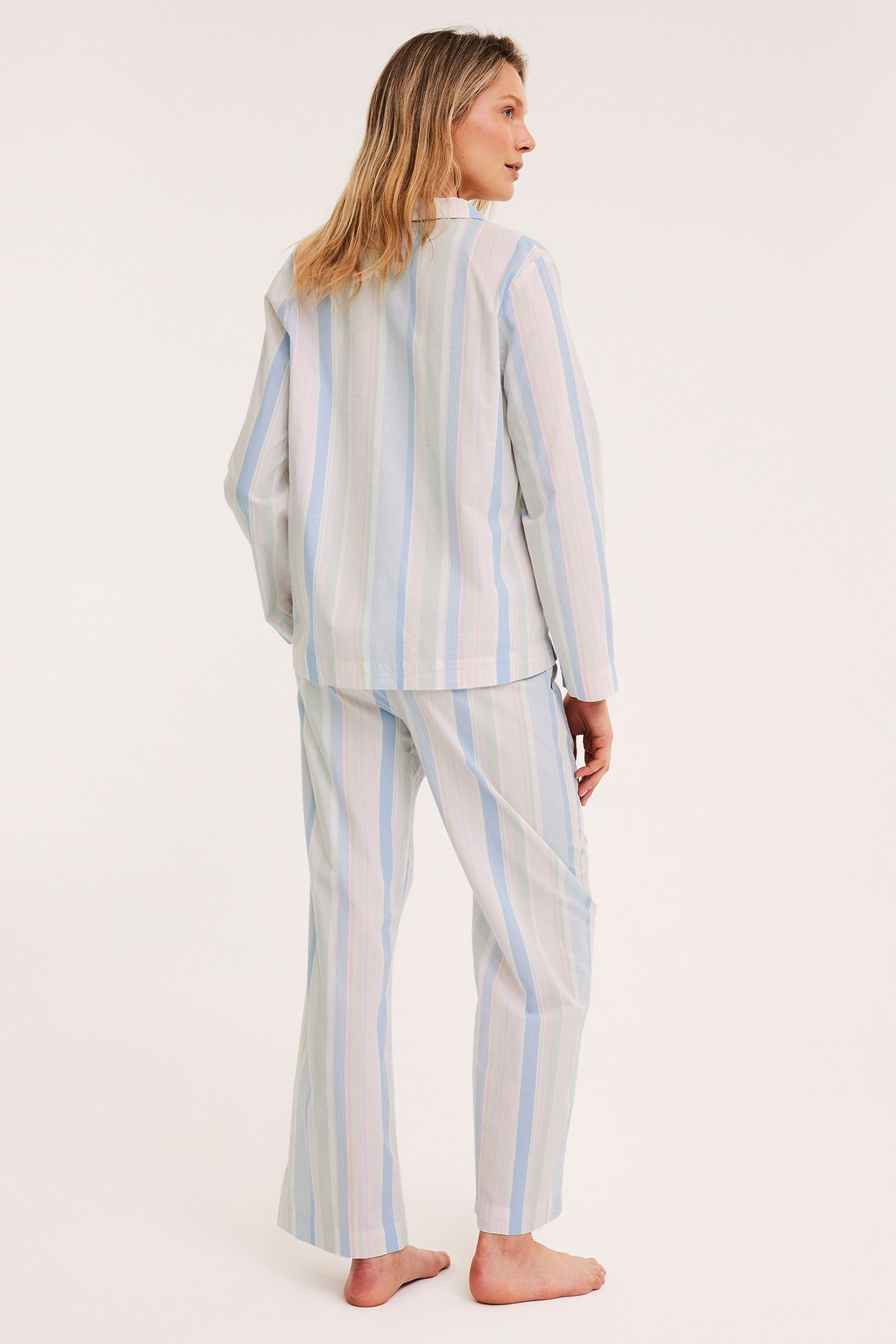 Rygg-sidebilde av en kvinne i et blått, hvitt og lysegrønt stripet pyjamasett i vevd bomull.