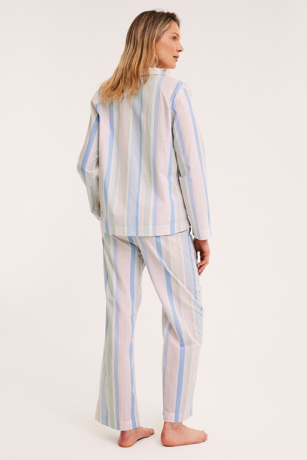 Widok z tyłu: kobieta w niebiesko-różowo-zielonych pasiastych bawełnianych spodniach piżamowych i pasującej koszuli.