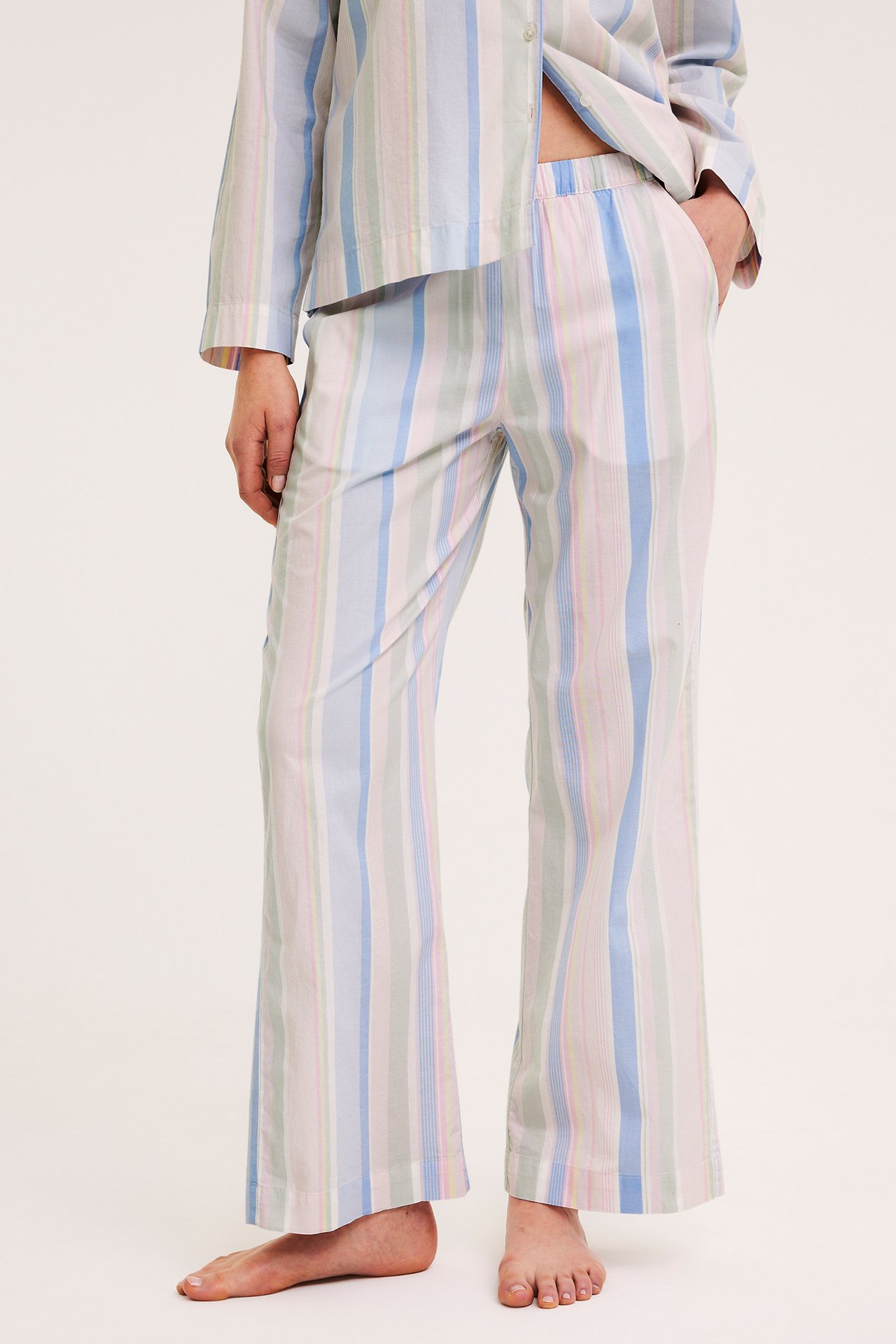 Edestä näkymä: nainen yllään pastellisävyiset moniraitaiset puuvillapyjamahousut joustovyötäröllä ja yhteensopiva toppi.
