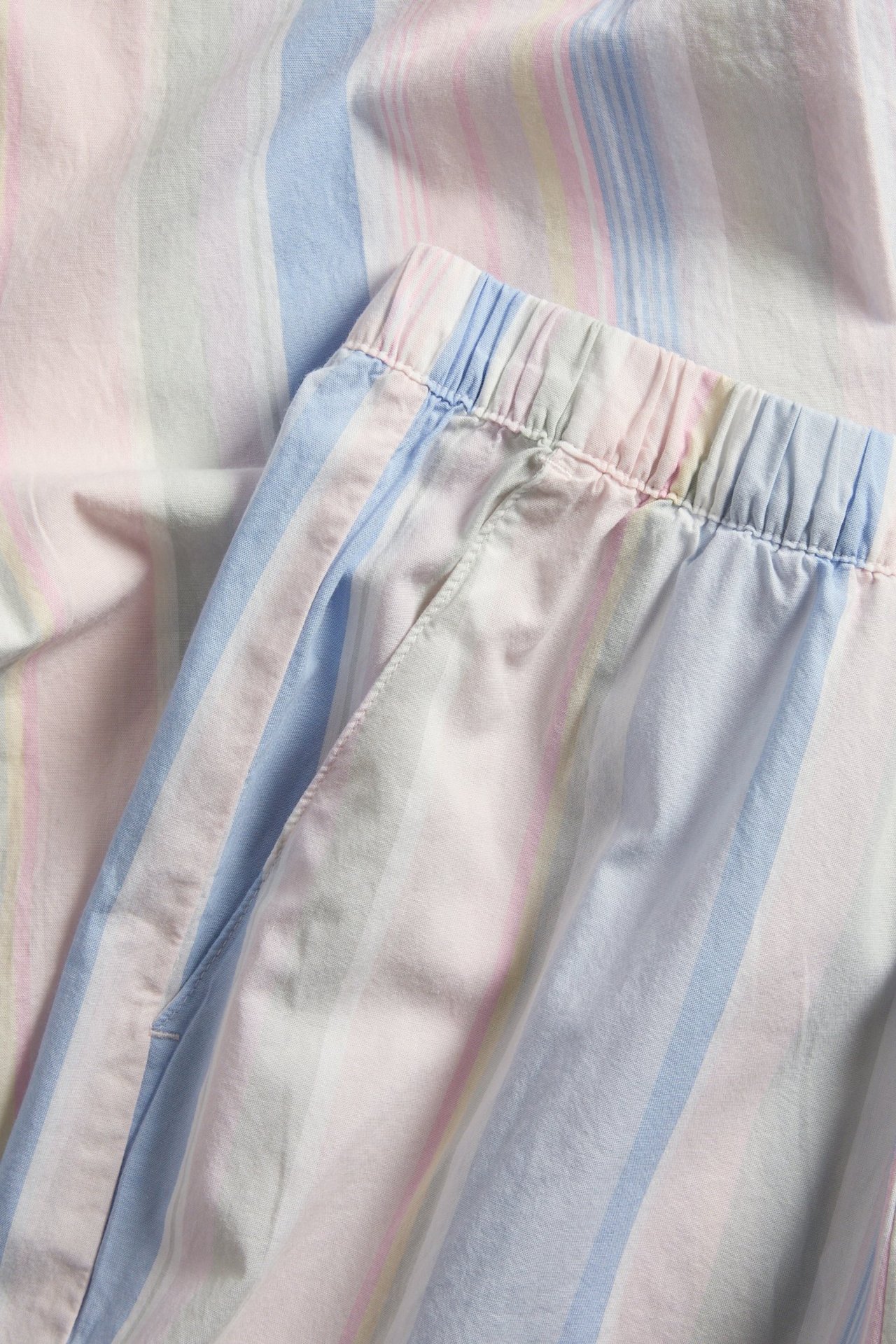 Zbliżenie na pastelowe, w paski, tkane bawełniane spodnie piżamowe z elastyczną talią i kieszeniami.