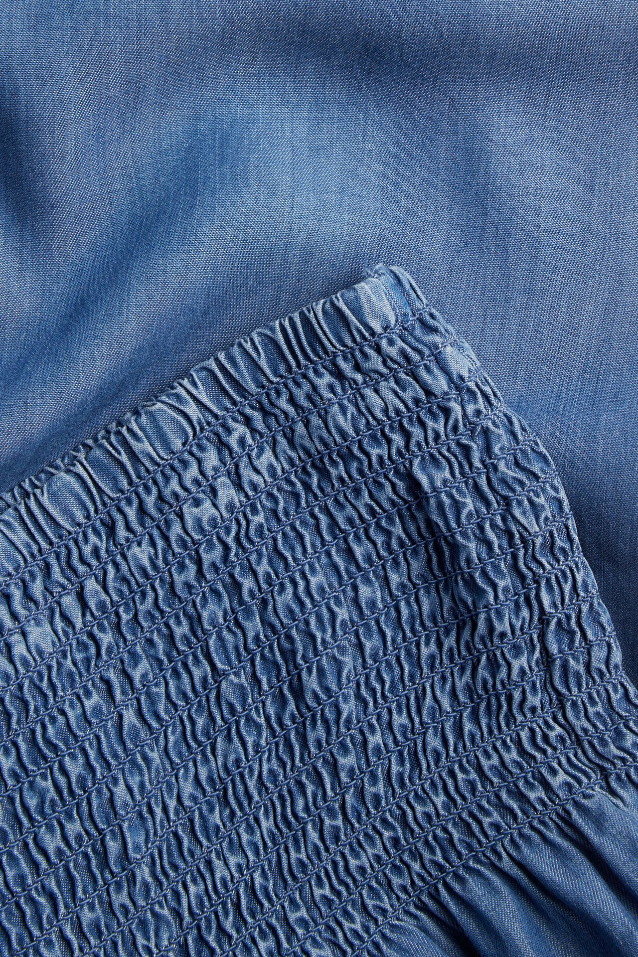 Lähikuva vaaleansinisistä lyocell-housuista, joissa on smokkausvyötärö.