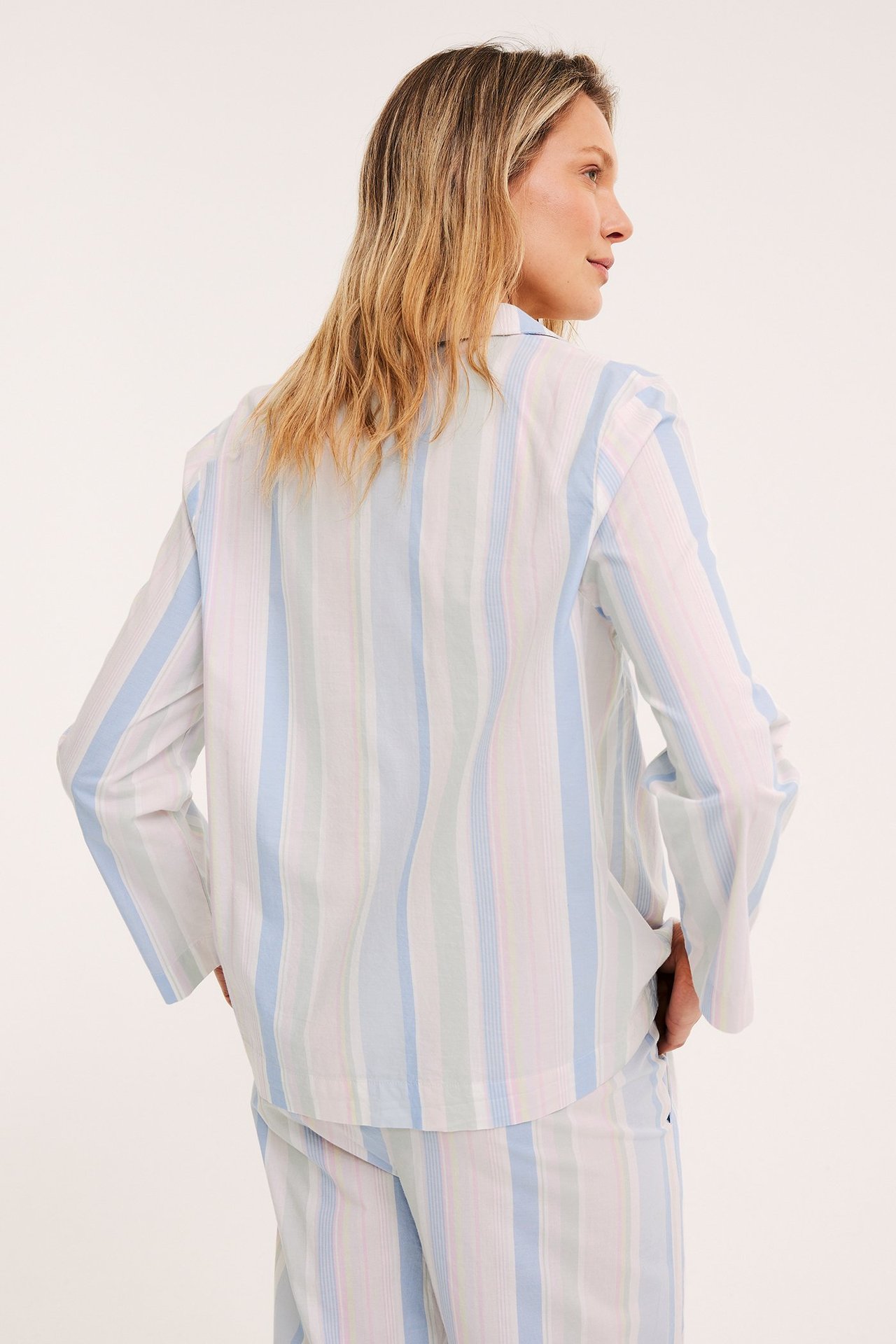 Nainen takaa, yllään pastelliraidallinen puuvillapyjamapaita ja yhteensopivat housut.