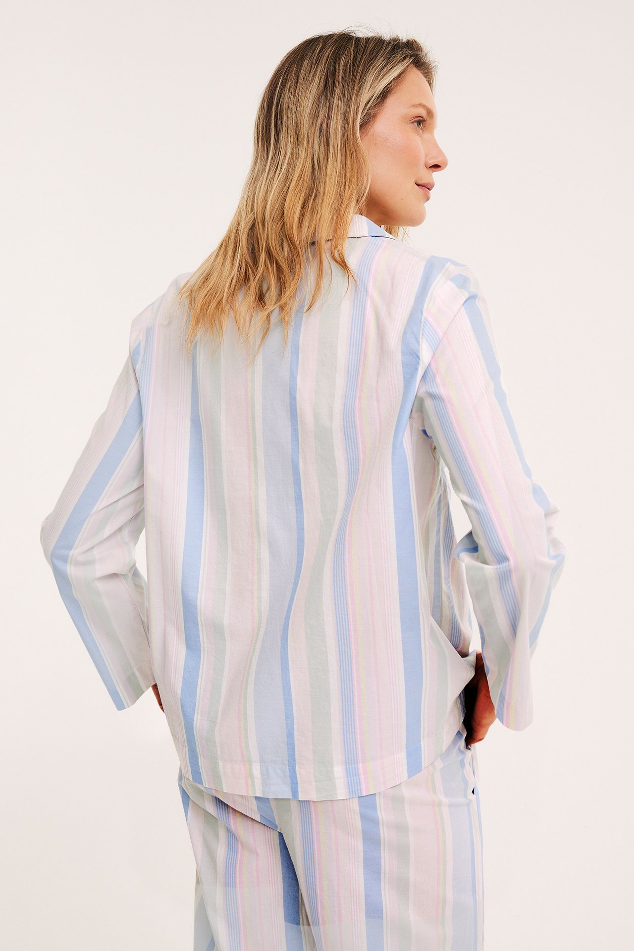 Bakre sidovy av kvinna i randig pyjamasskjorta i bomull och matchande byxor.