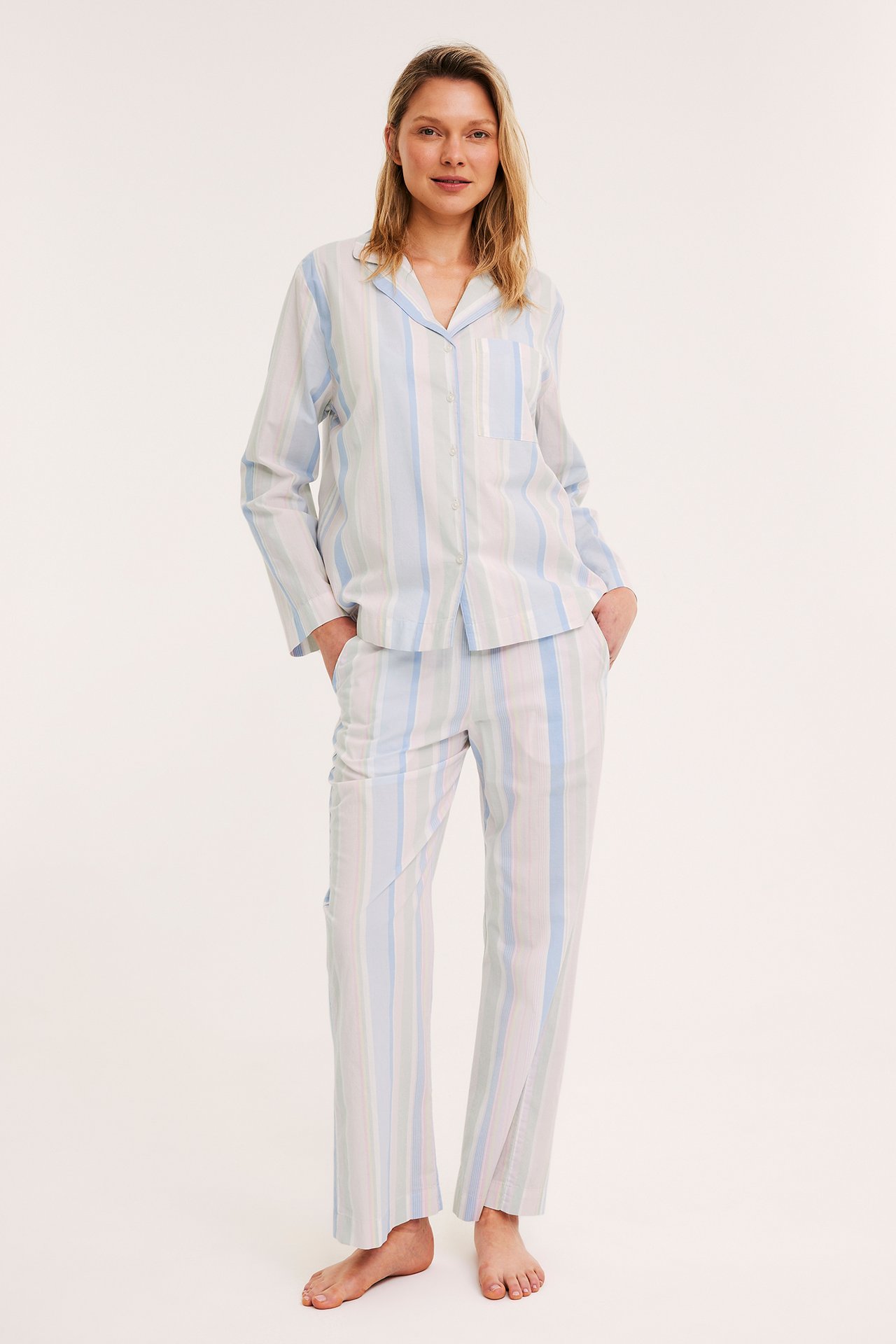 Naisen etukuva sinivalko- ja vaaleanvihreäraitaista puuvillapyjamapaitaa ja siihen sopivia housuja.