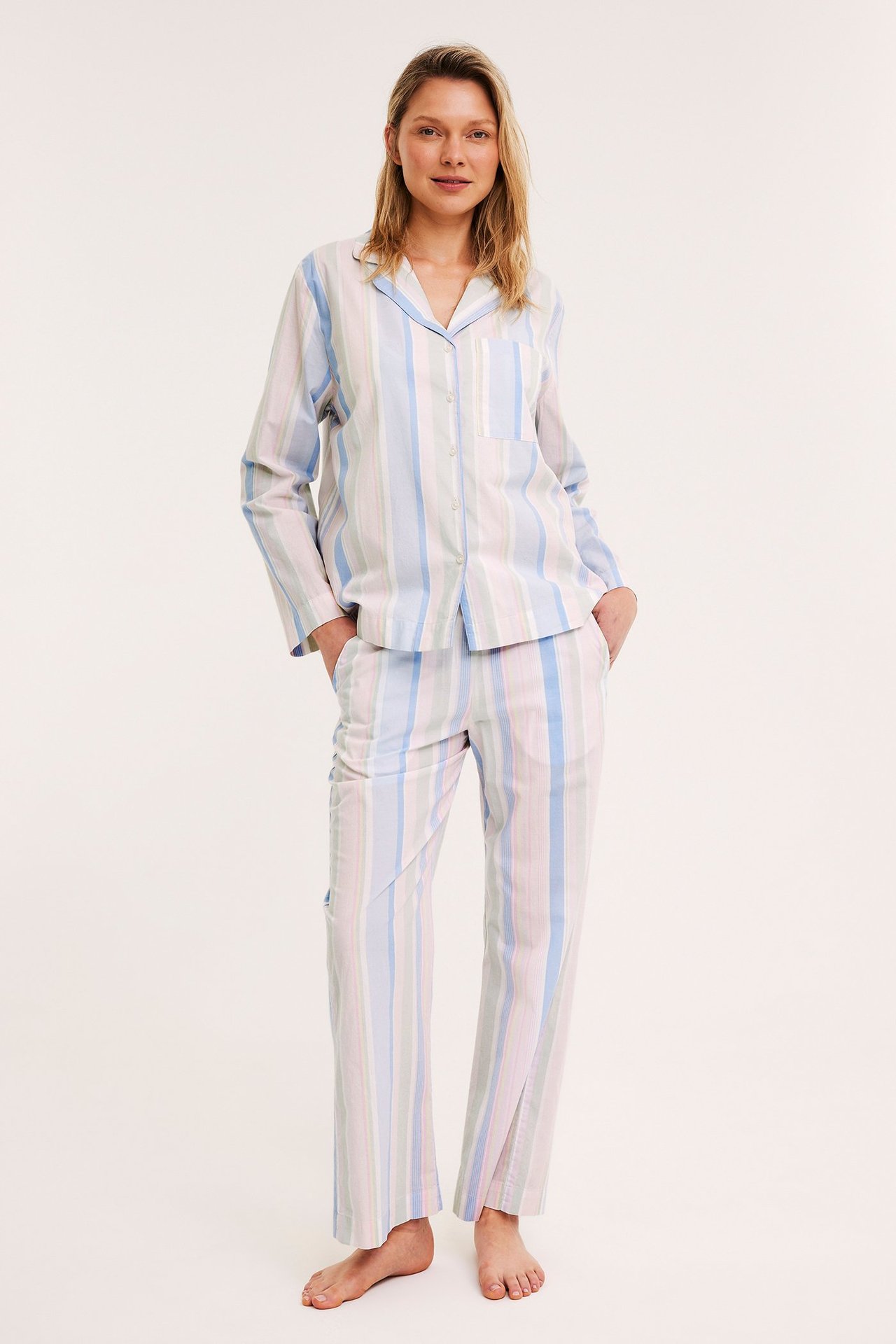 Framifrån, en kvinna i randig pyjamasskjorta av vävd bomull med matchande långbyxor.