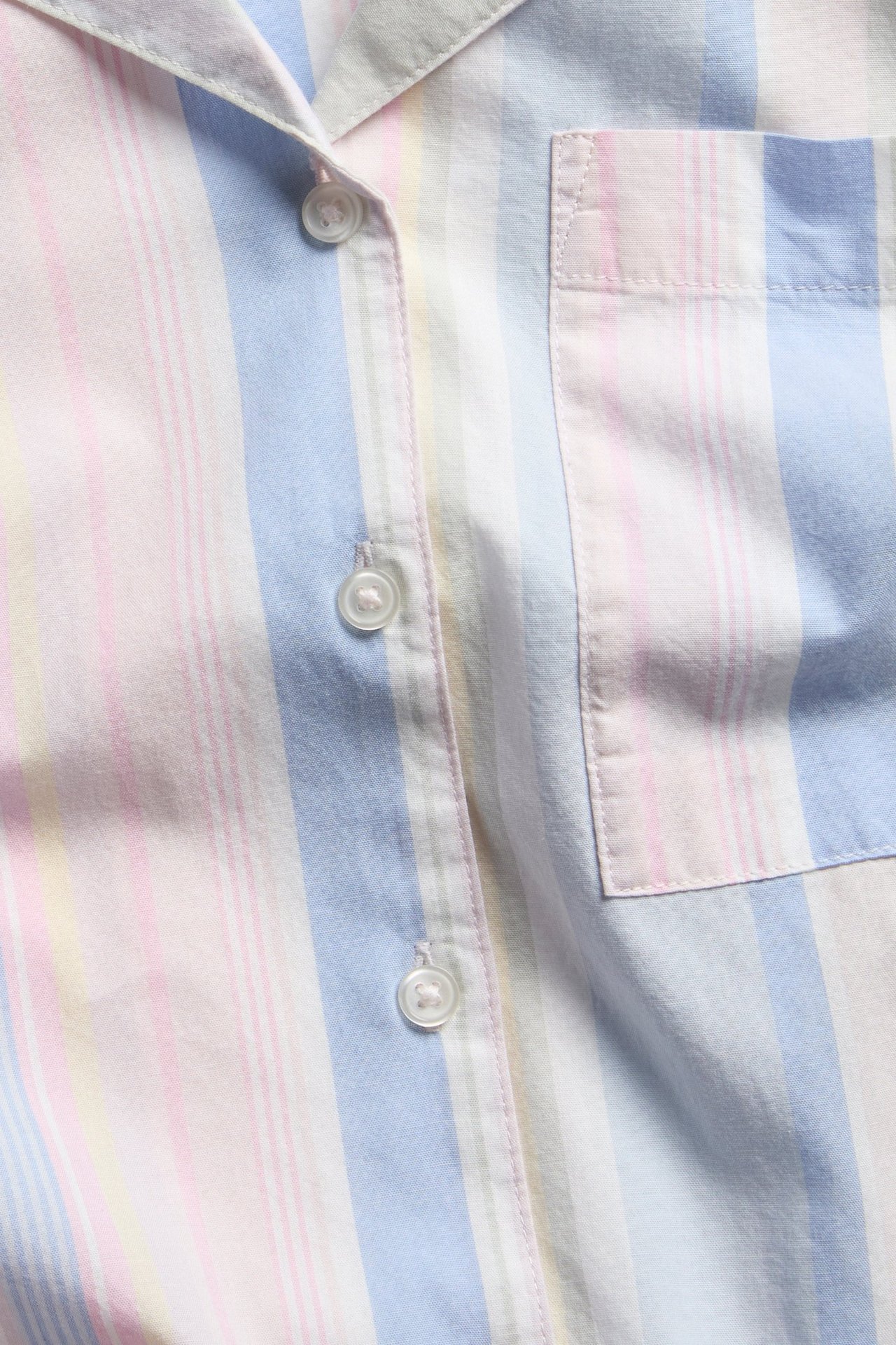 Lähikuva edestä pastellivärisestä raidallisesta puuvillapyjamapaidasta, jossa on valkoiset napit ja rintatasku.