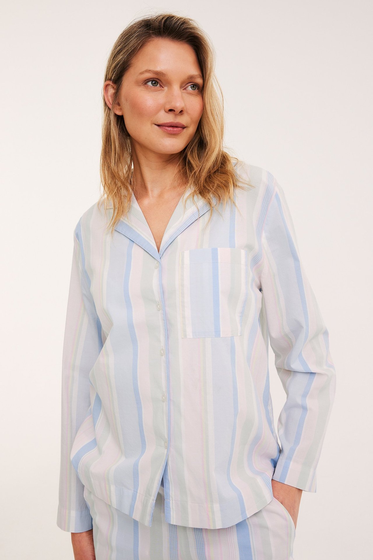 Forfra: kvinne i blåstripet vevd bomullspysjamas skjorte med krage, lomme og matchende pysjamasbukser.