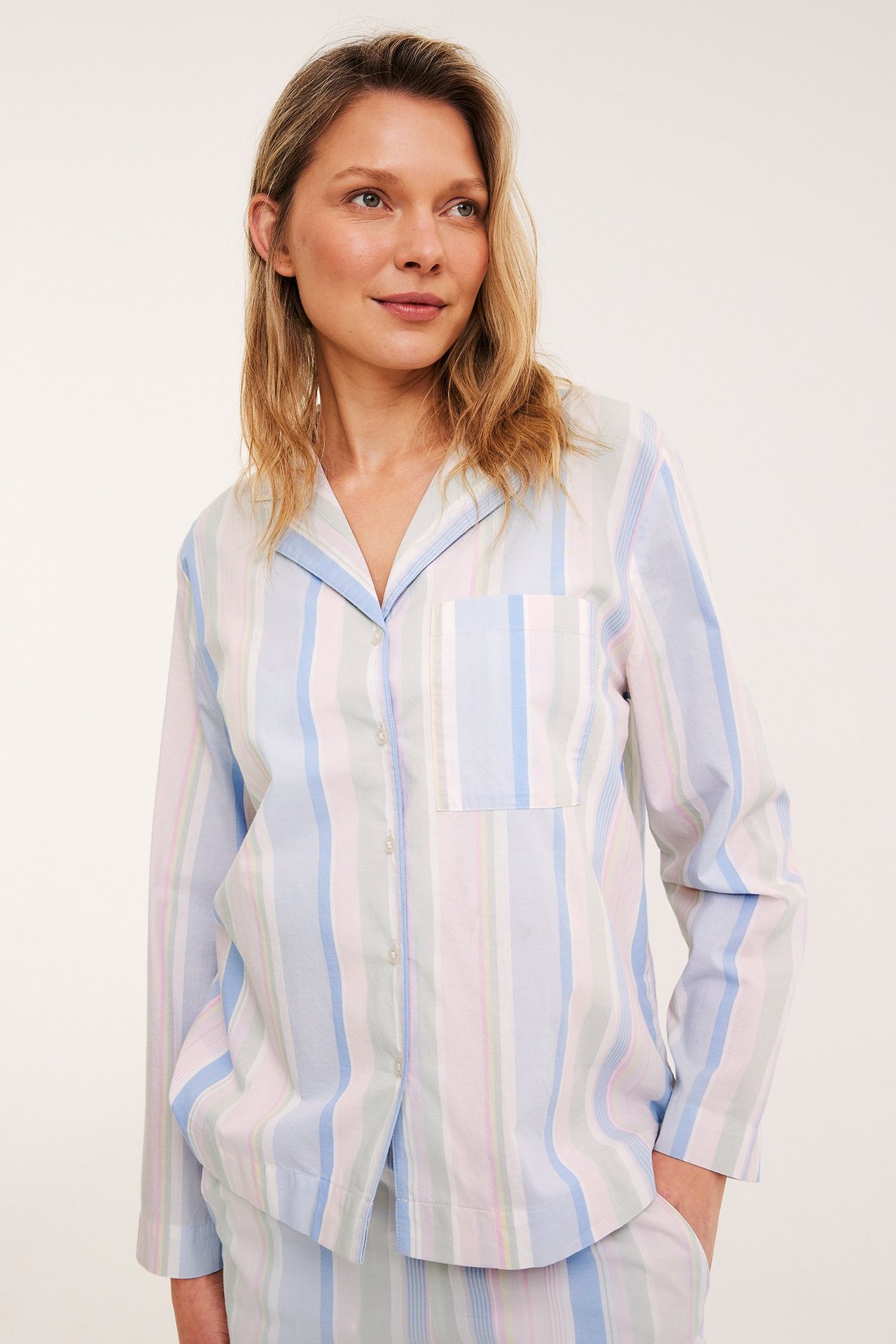 Frontutsikt: kvinne i lys flerfarget stripet pyjamasskjorte i bomull med krage, brystlomme og matchende bukser.