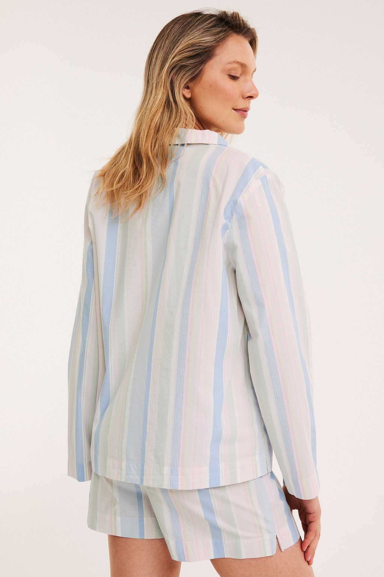 Bakfra av kvinne i blå, grønn, rosa stripete bomulls-pyjamasshorts og matchende skjorte.
