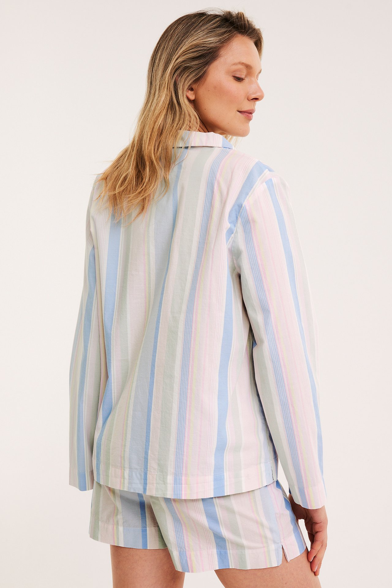 Baksidesvy av en kvinna i randigt pyjamasset av vävd bomull med blå, rosa, gröna ränder.