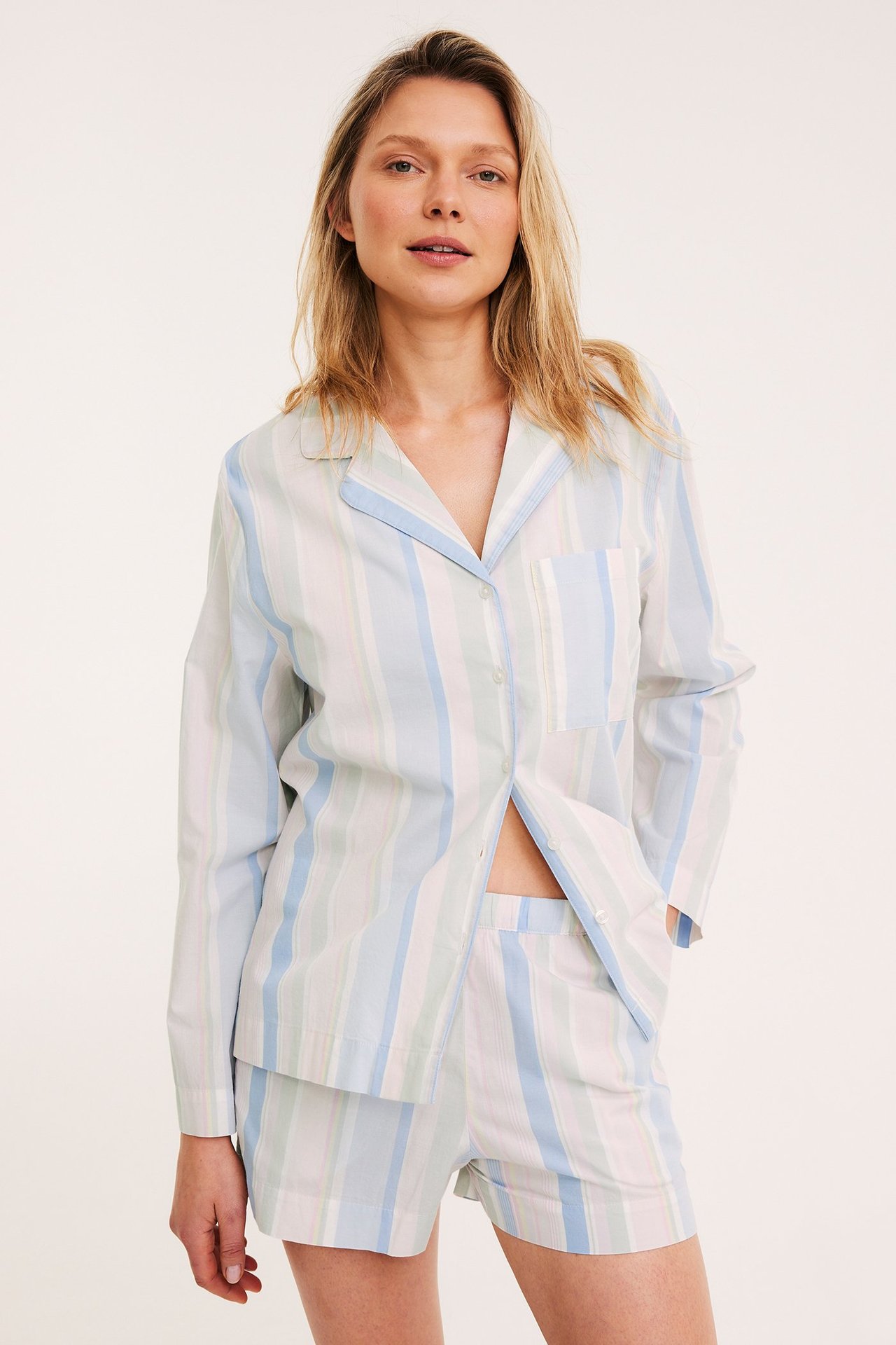 Frontutsikt av kvinne i lyse pastellstripete pyjamasshorts i bomull og matchende skjorte.
