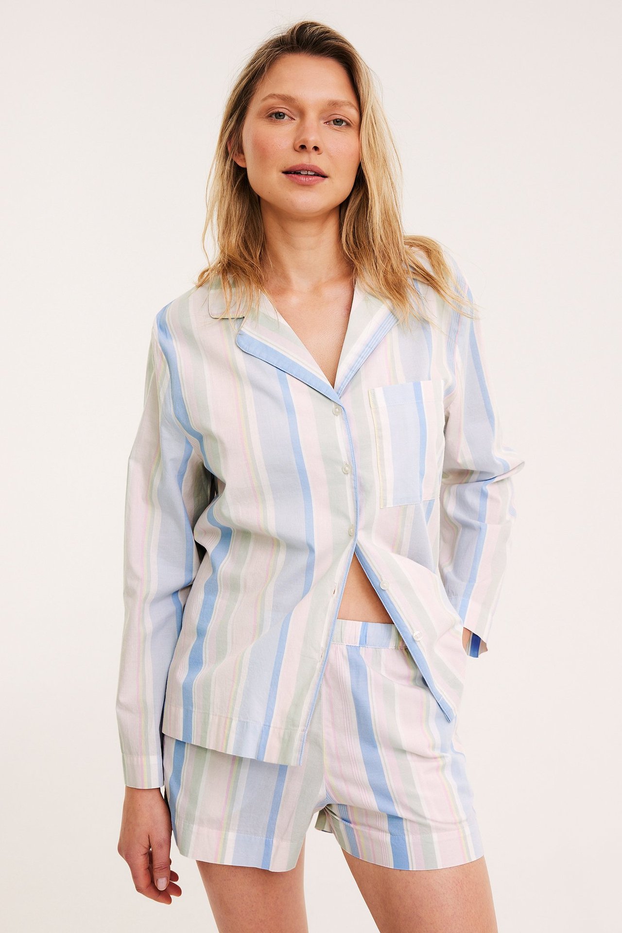 Edestä: Nainen raidallisissa puuvillapyjamashortseissa ja paidassa. Värit: sininen, pinkki, vihreä, valkoinen.