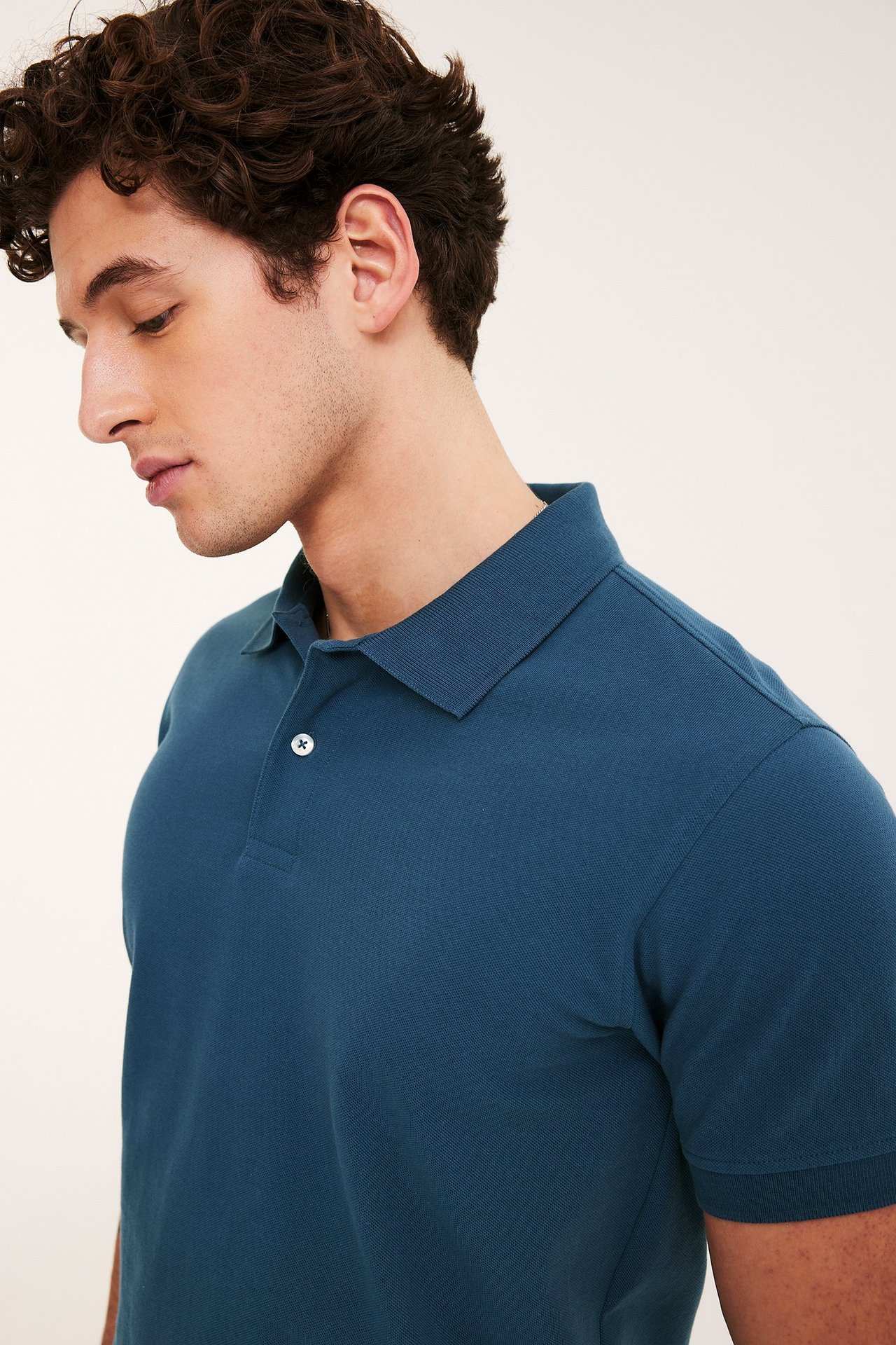 Närbild i sidoprofil på en man i mörkblå bomullspikétröja med två vita knappar.