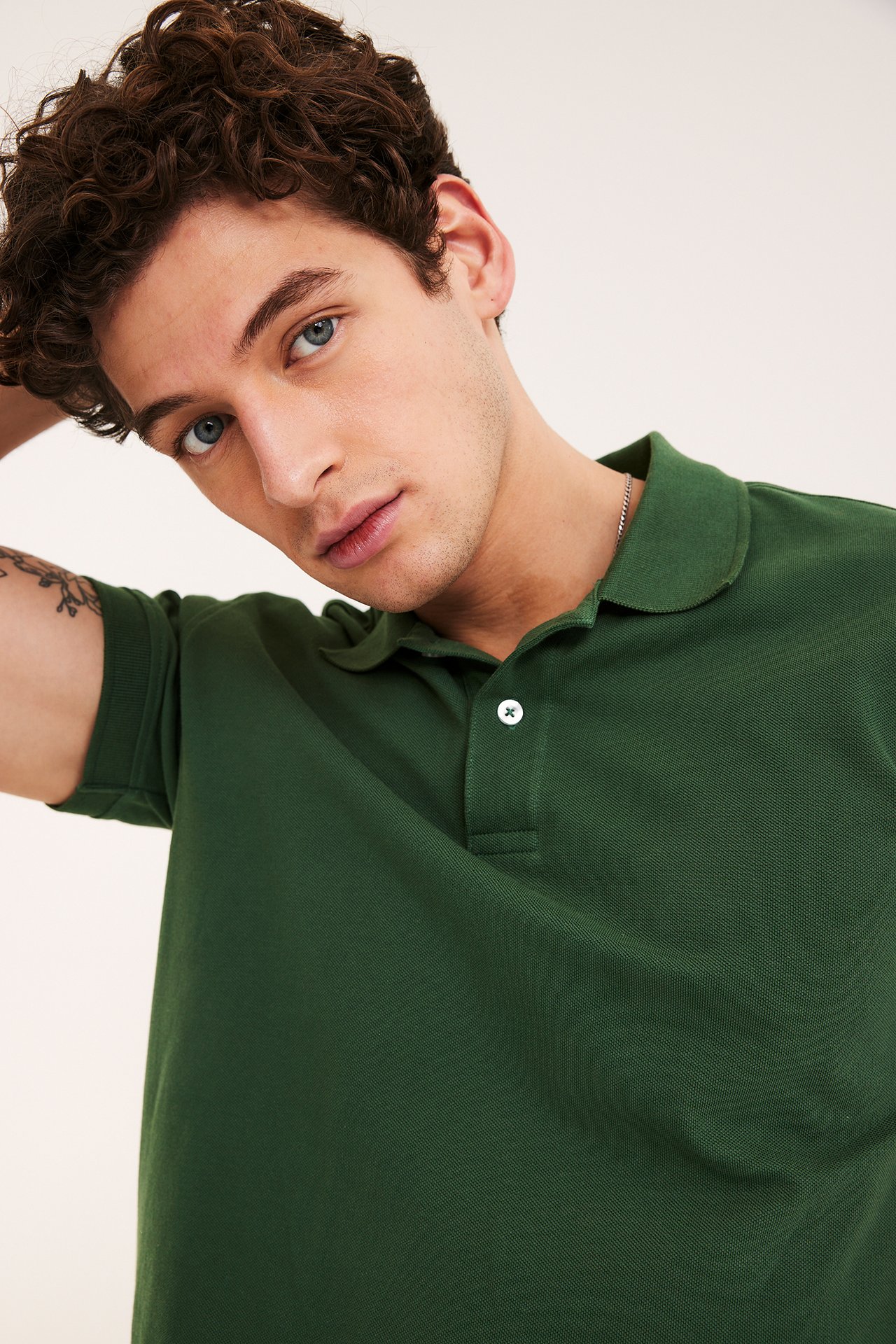 Närbild framifrån av en man i en enfärgad grön pikétröja i bomull med två vita knappar.