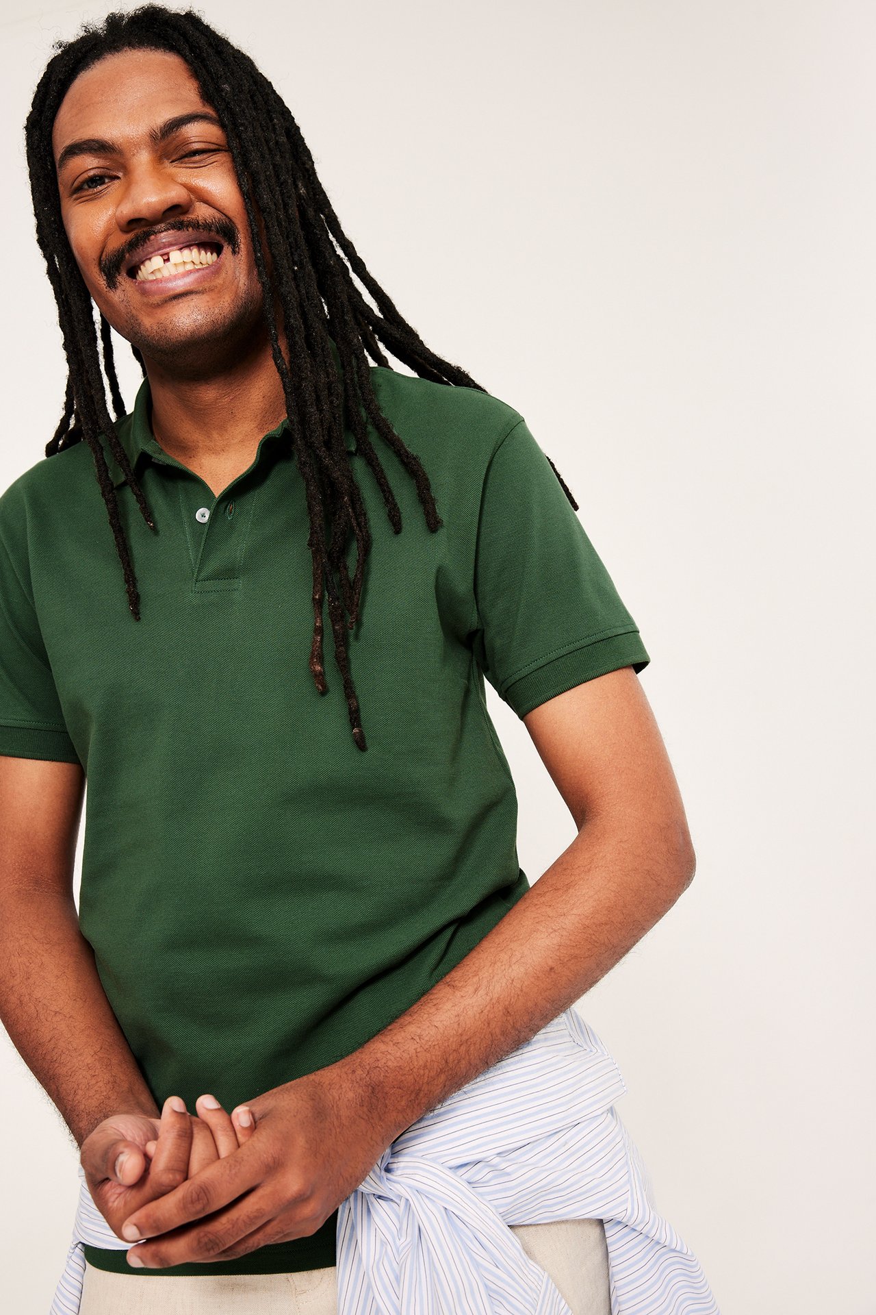 Mann i grønn bomullspiké med to knapper. Stripete skjorte knyttet i midjen, frontvisning.