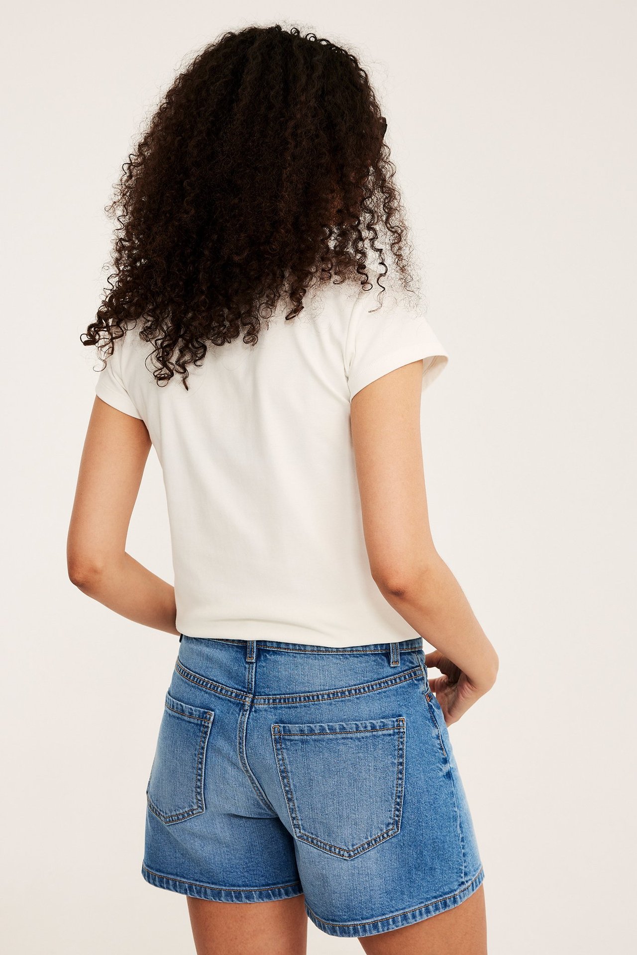 Ryggvy av en kvinna i ljusblå denimshorts med bakfickor och en enkel vit t-shirt.