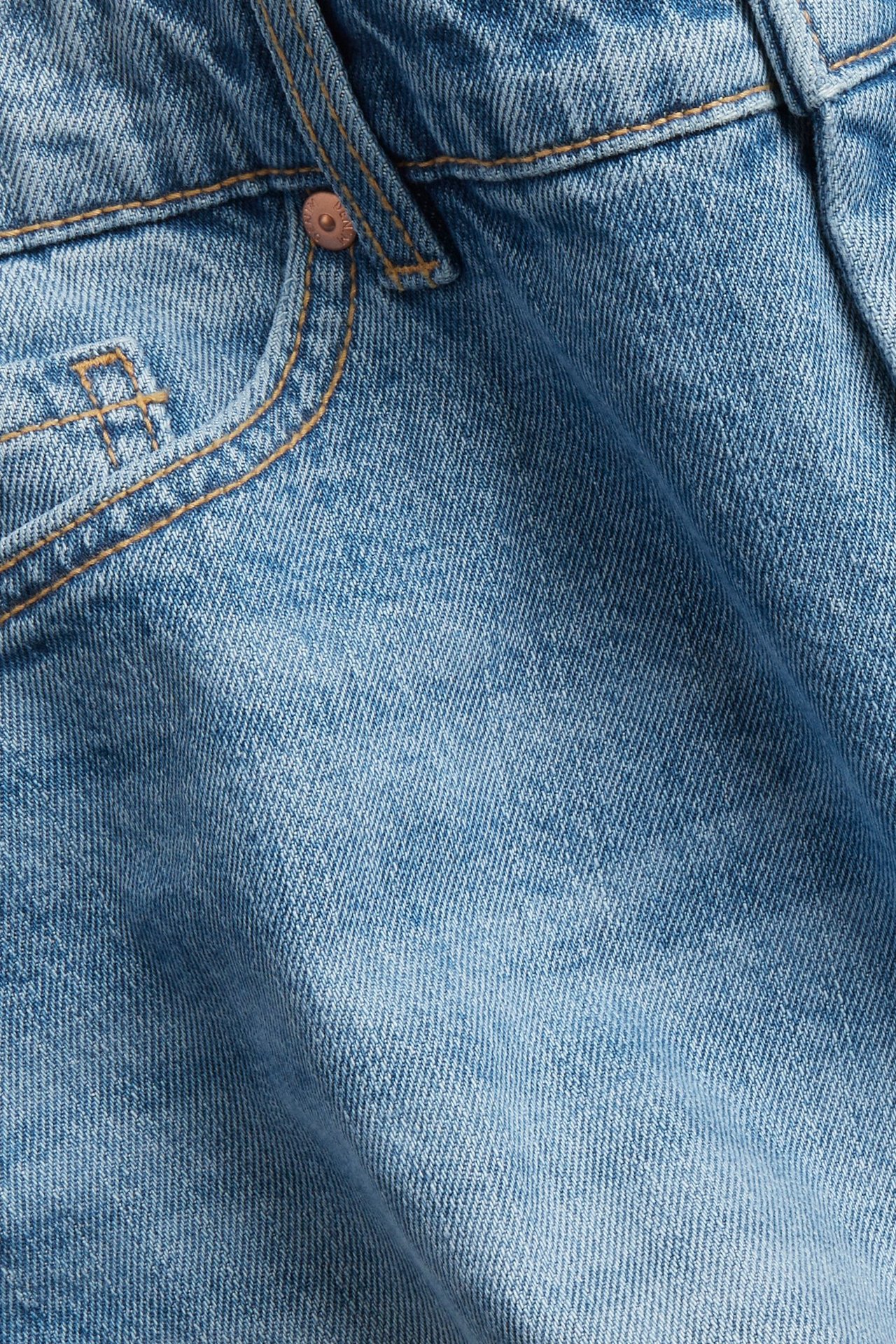 Närbild, framifrån, av ljusblå denimshorts med ficka och en kopparnit.