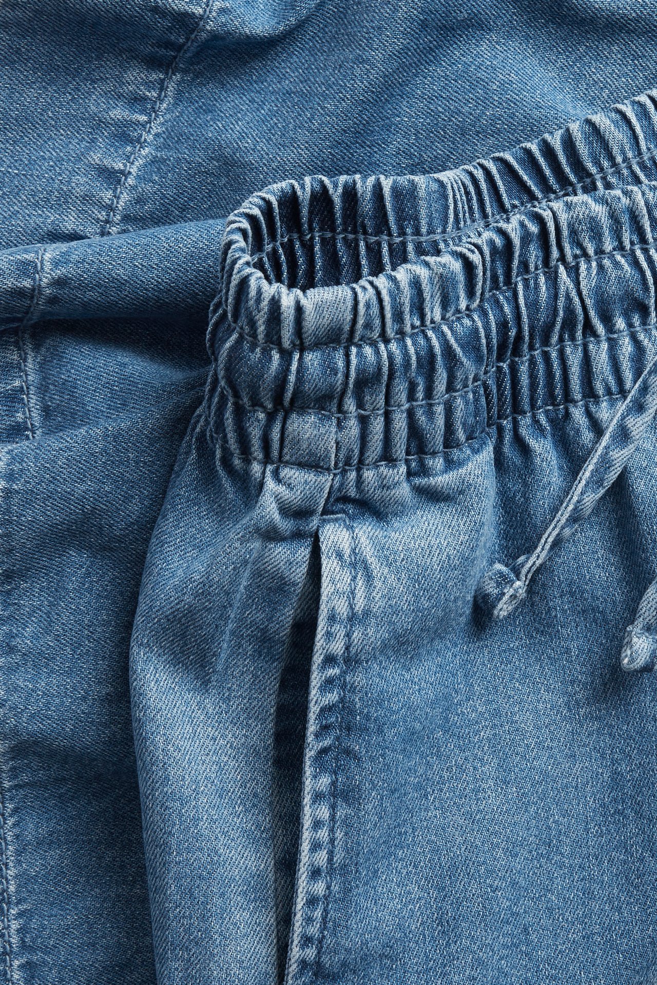 Lähikuva vaaleansinisistä denim-shortseista, joissa joustava kiristysnyörillinen vyötärö.