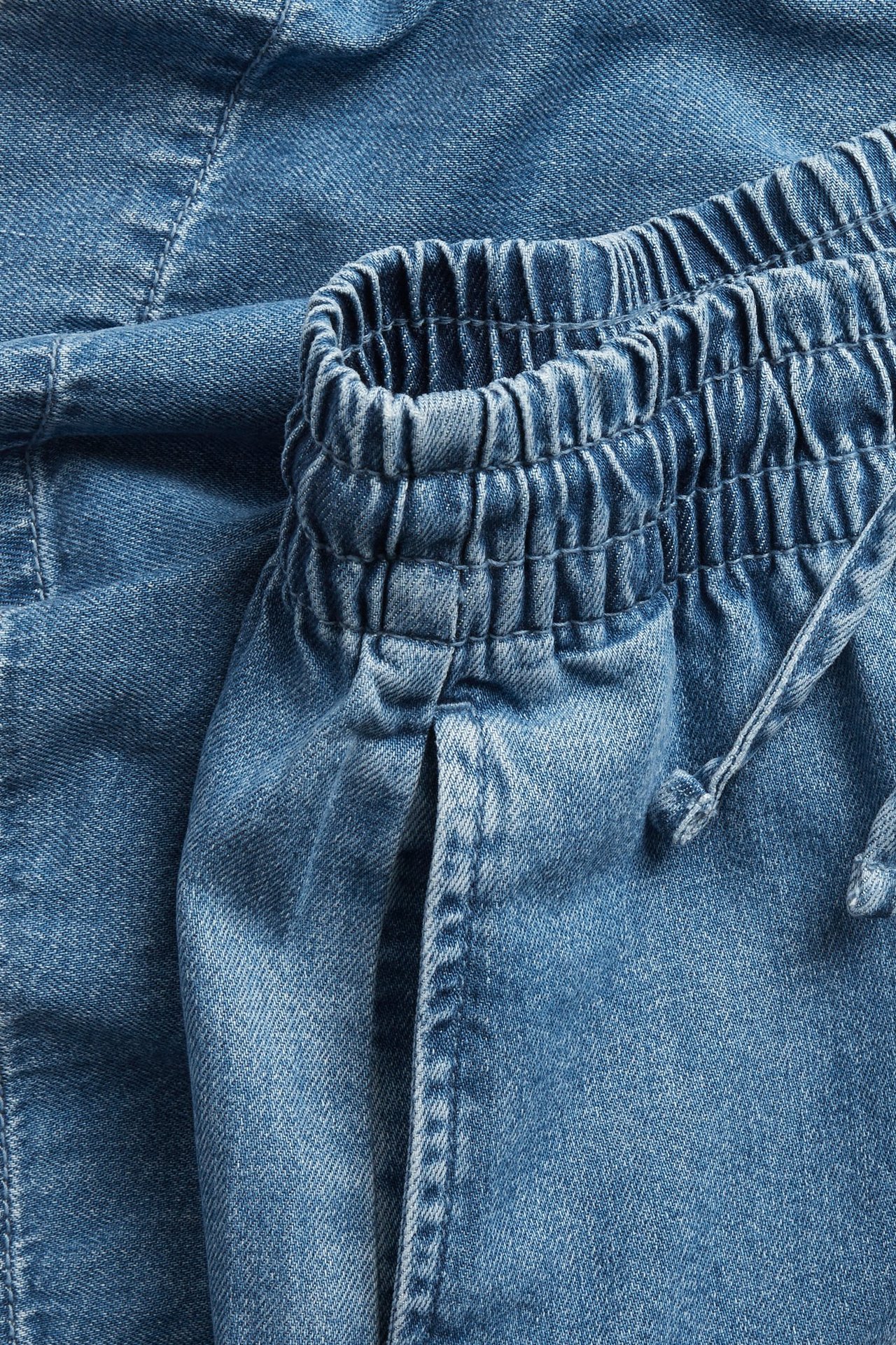 Närbild av ljusblå jeansshorts med elastisk midja och dragsko.