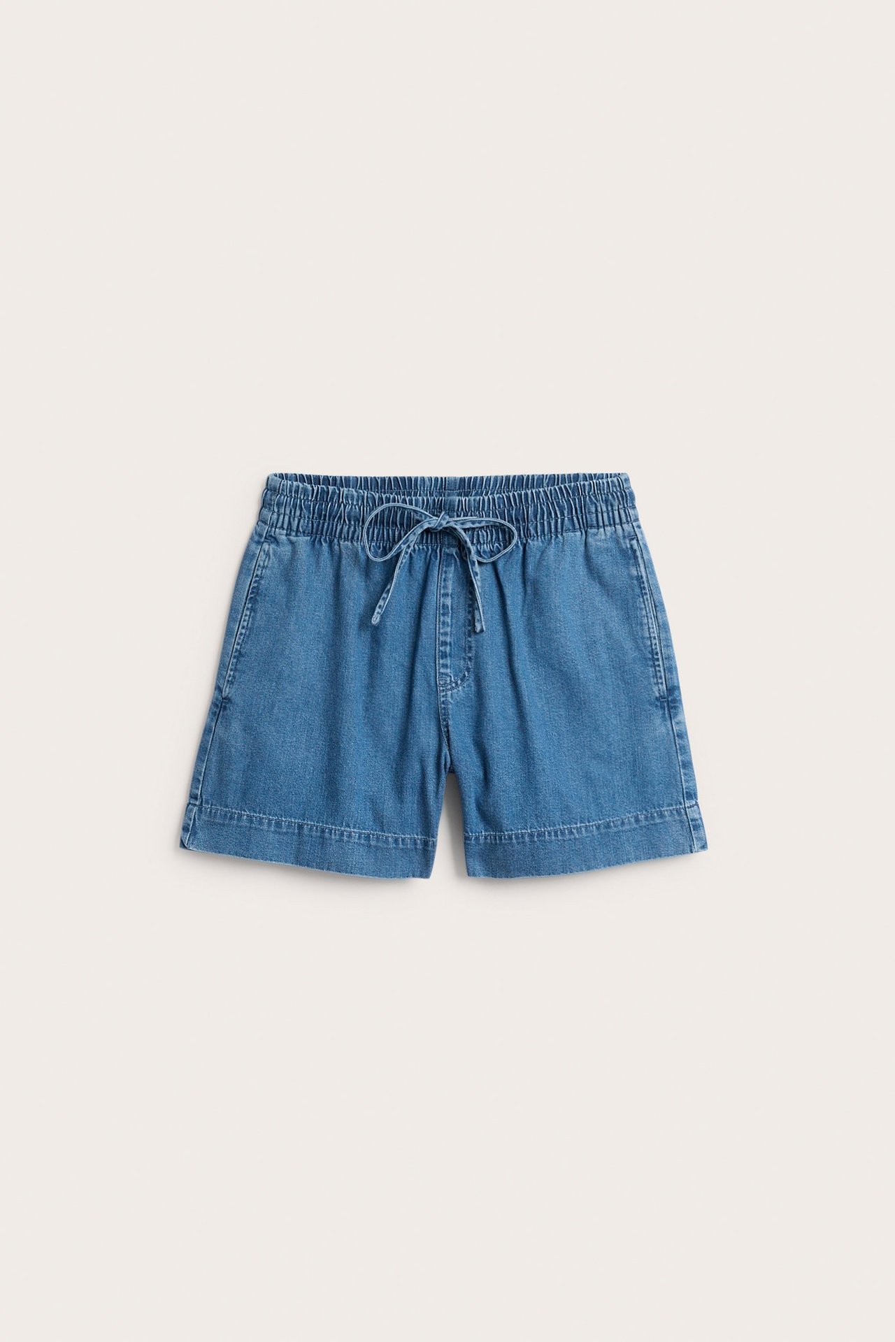 Framifrån, enfärgade denimblå pull-on jeansshorts med resårlinning och dragsko framtill.