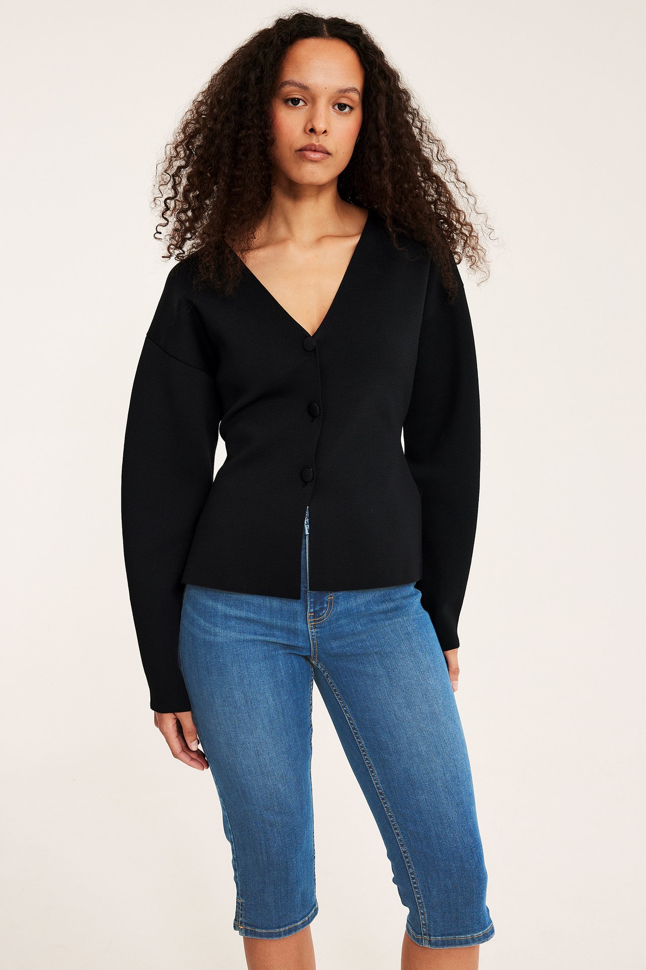Widok z przodu: kobieta w niebieskich dżinsowych spodniach capri i czarnym zapinanym topie z dekoltem V.