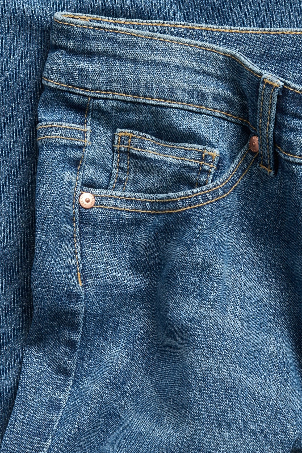 Närbild av blå caprijeans i denim med framficka, linning och bronnit.