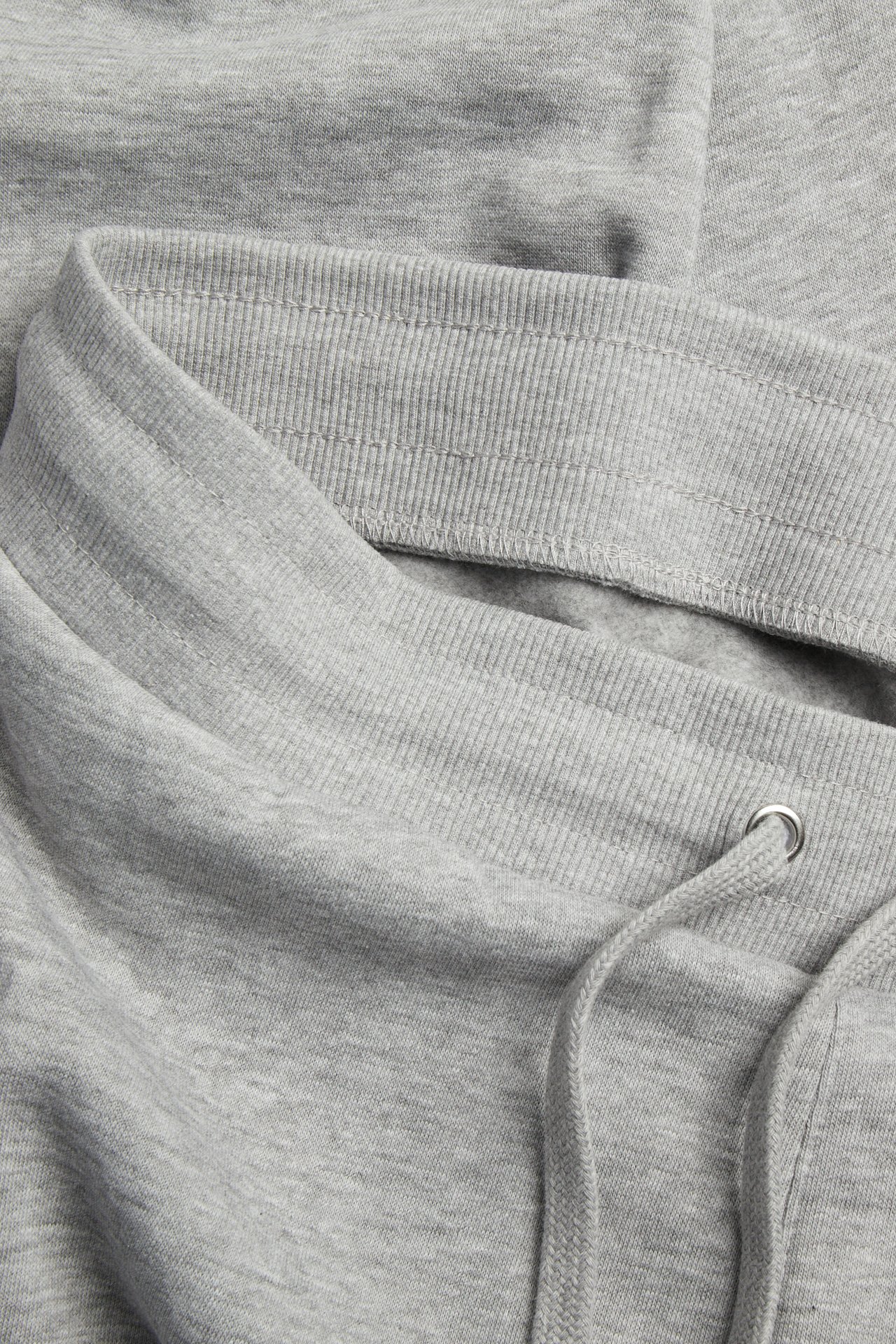 Lähikuva vaaleanharmaameleeratuista collegehousuista, joissa joustava ribbivyötärö ja kiristysnyöri.