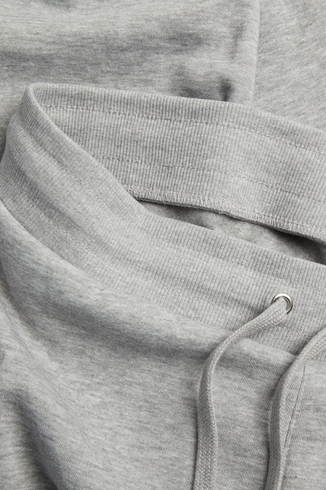 Närbild av ljusgråmelerade sweatpants med elastisk ribbad midja och synlig dragsko.
