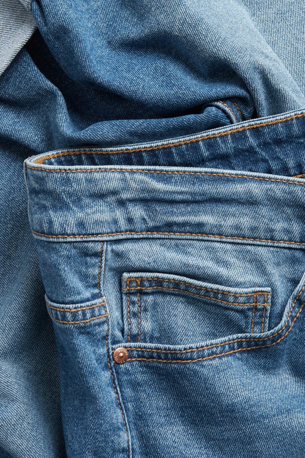 Zbliżenie na niebieskie szorty jeansowe z paskiem, przednią kieszenią, pomarańczowymi przeszyciami i miedzianym nitem.