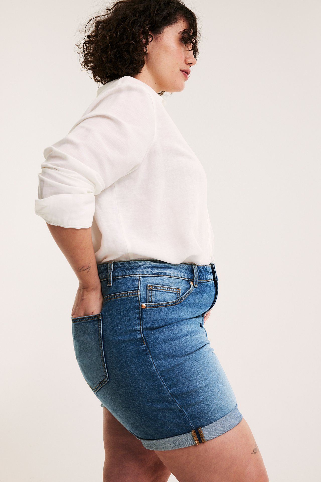 Naisen sivukuva, yllään siniset käännetyt farkkushortsit ja valkoinen pitkähihainen paita.