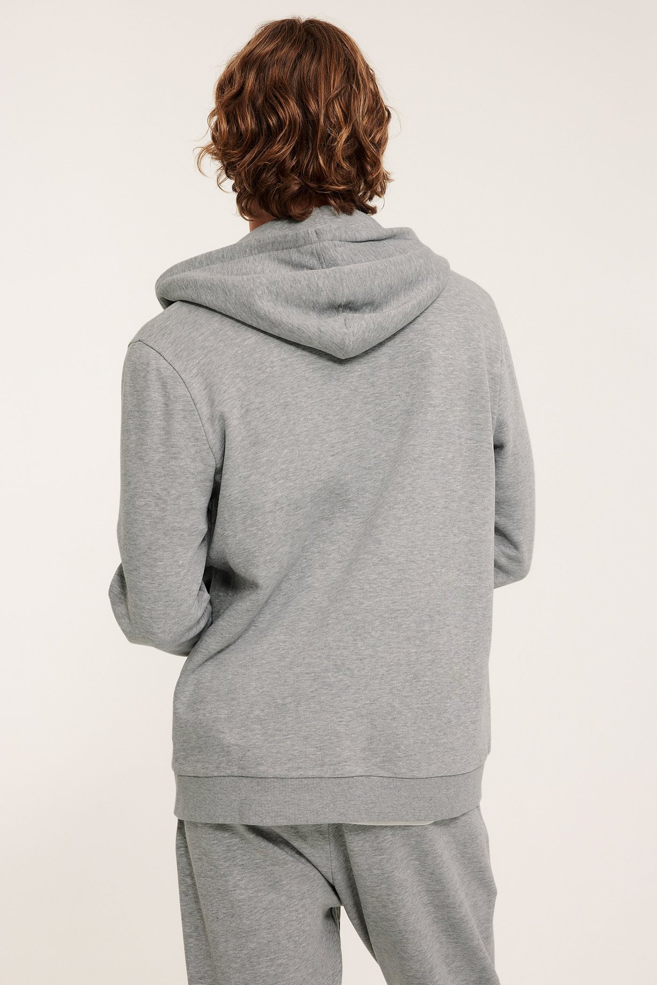 Mies takaa, vaaleanharmaa vetoketjuhuppari kiristysnyörihupulla ja yhteensopivat collegehousut.