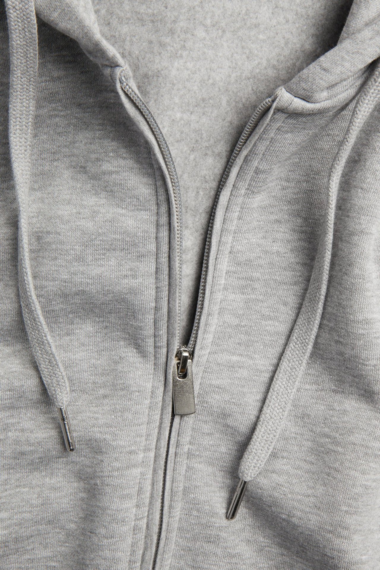 Zbliżenie męskiej jasnoszarej melanżowej bluzy z kapturem, z zamkiem błyskawicznym i sznurkami kaptura.