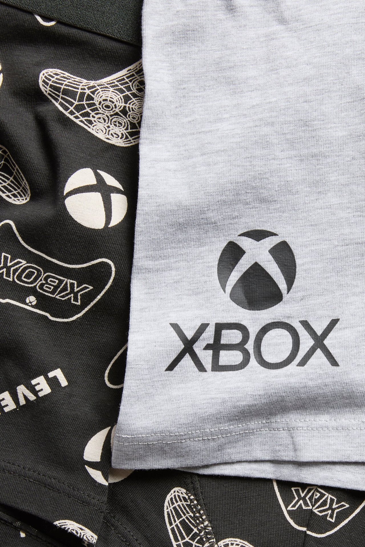 Lähikuva harmaasta paidasta mustalla Xbox-logolla ja tummanharmaista shortseista valkoisella Xbox-kuviolla.