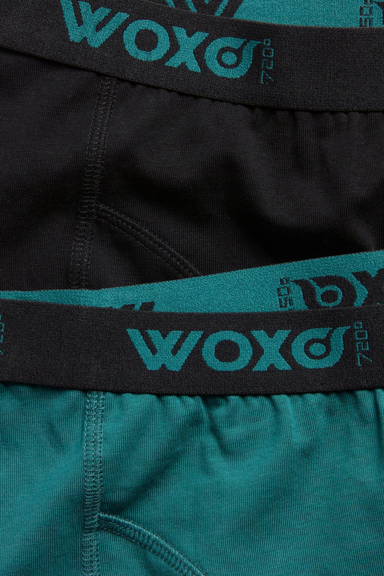 Närbild av två barnboxerkalsonger, en svart och en mörkgrön, med svarta WOXO-logoband i resåren.