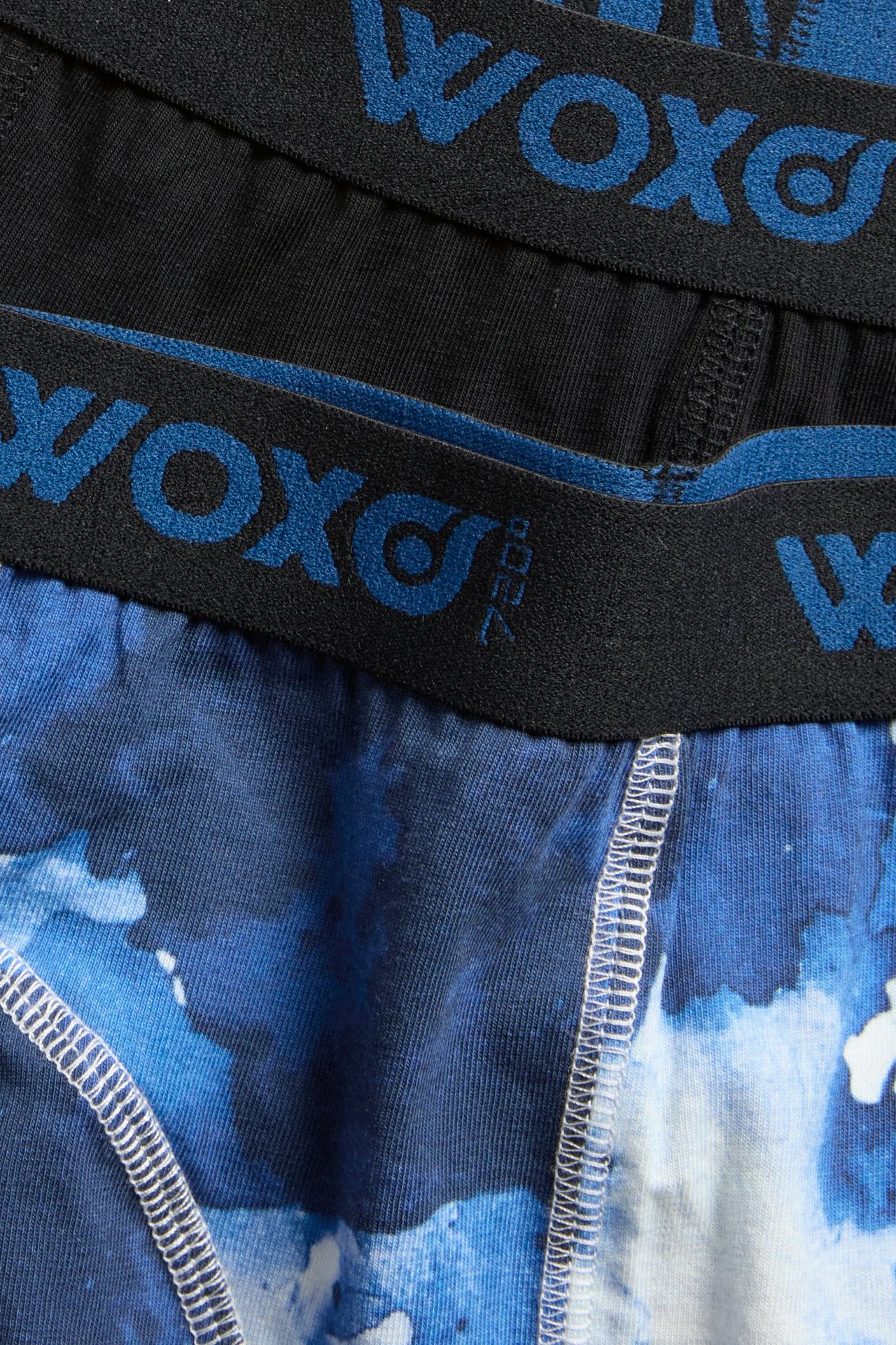 Zbliżenie dziecięcych bokserek: jedna para wzorzysta niebiesko-biała, druga czarna, z elastycznym pasem 'woxo'.